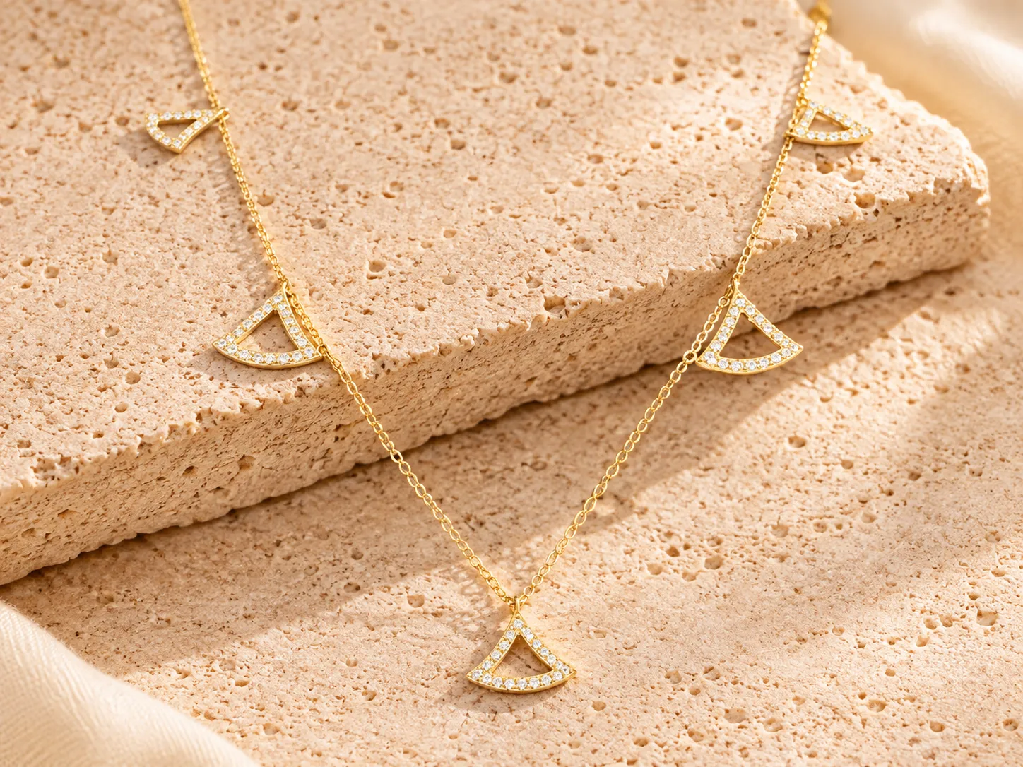 Fine gold chain with fan-shaped charms set with small clear stones, resting on a stone ledge