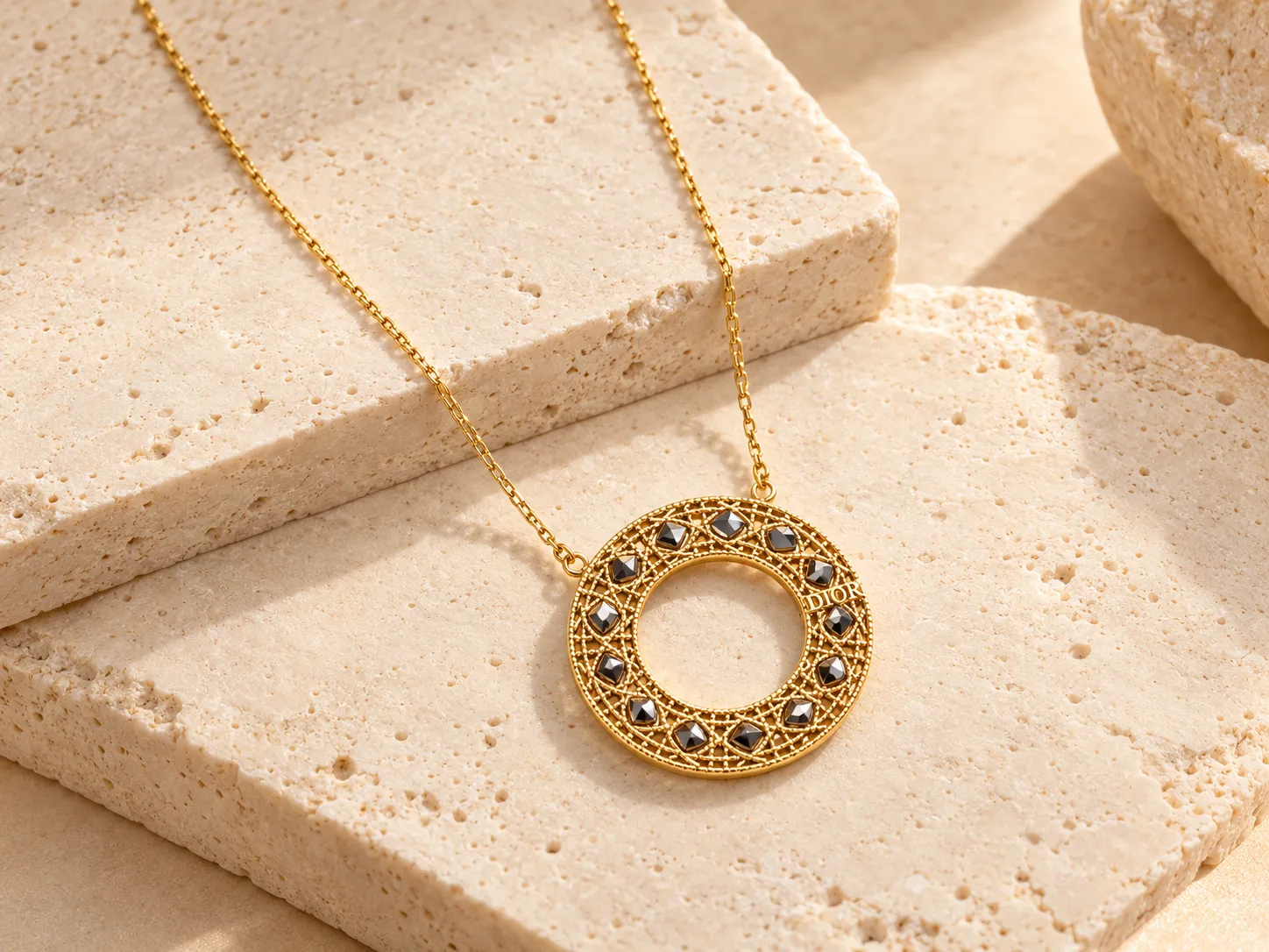 Gold necklace with a round openwork pendant with a lattice pattern and dark accents on a fine chain, resting on a stone ledge
