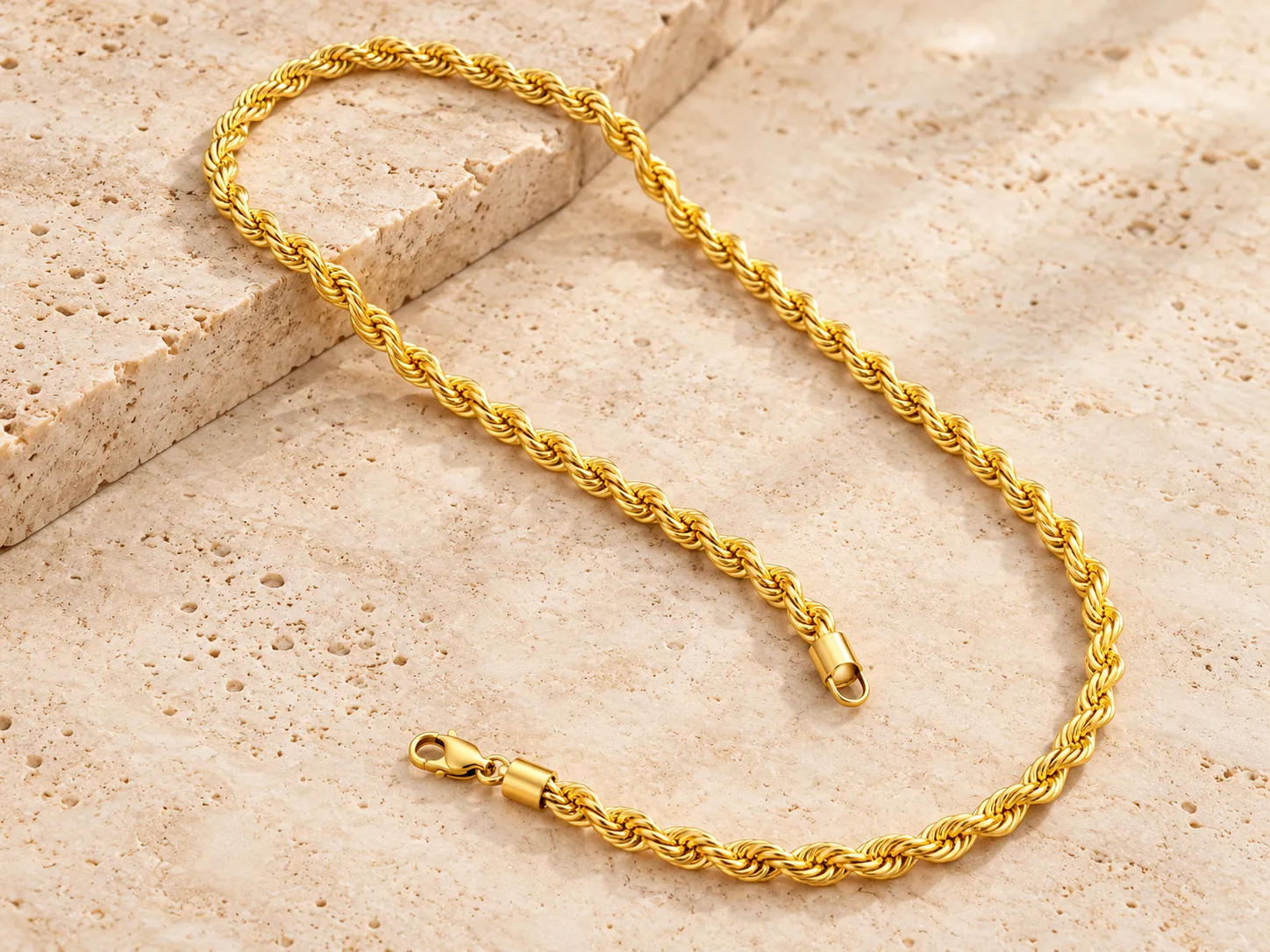 Gold twisted rope chain with a clasp, laid in a curve on a stone ledge