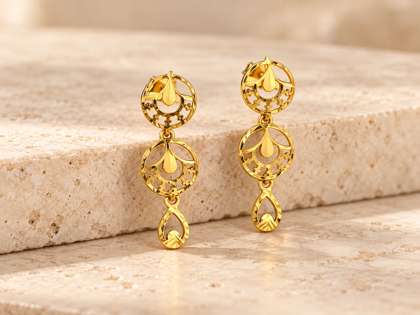 Gold earrings on a warm stone surface