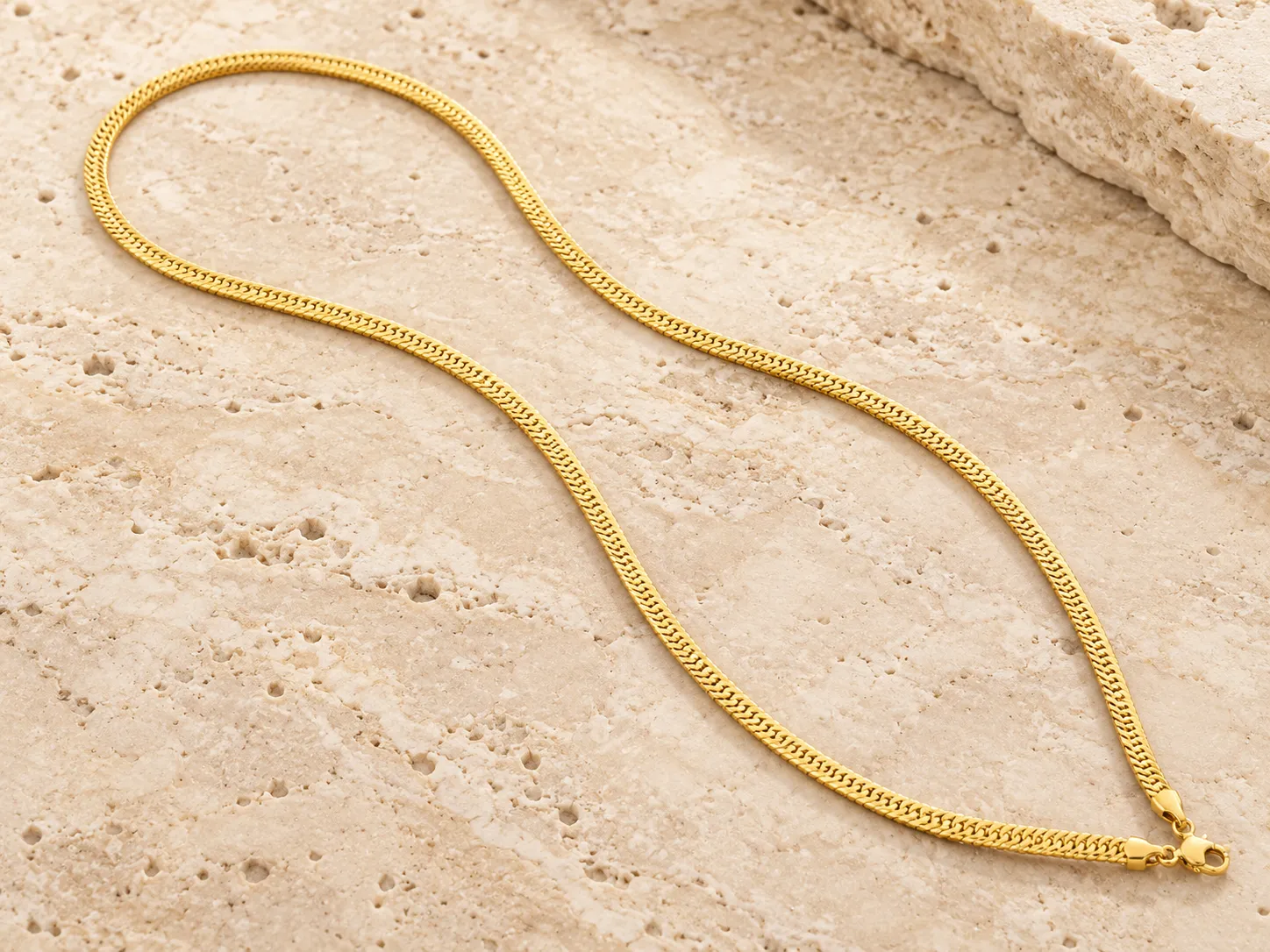 Slim gold chain laid in a gentle curve on a stone ledge