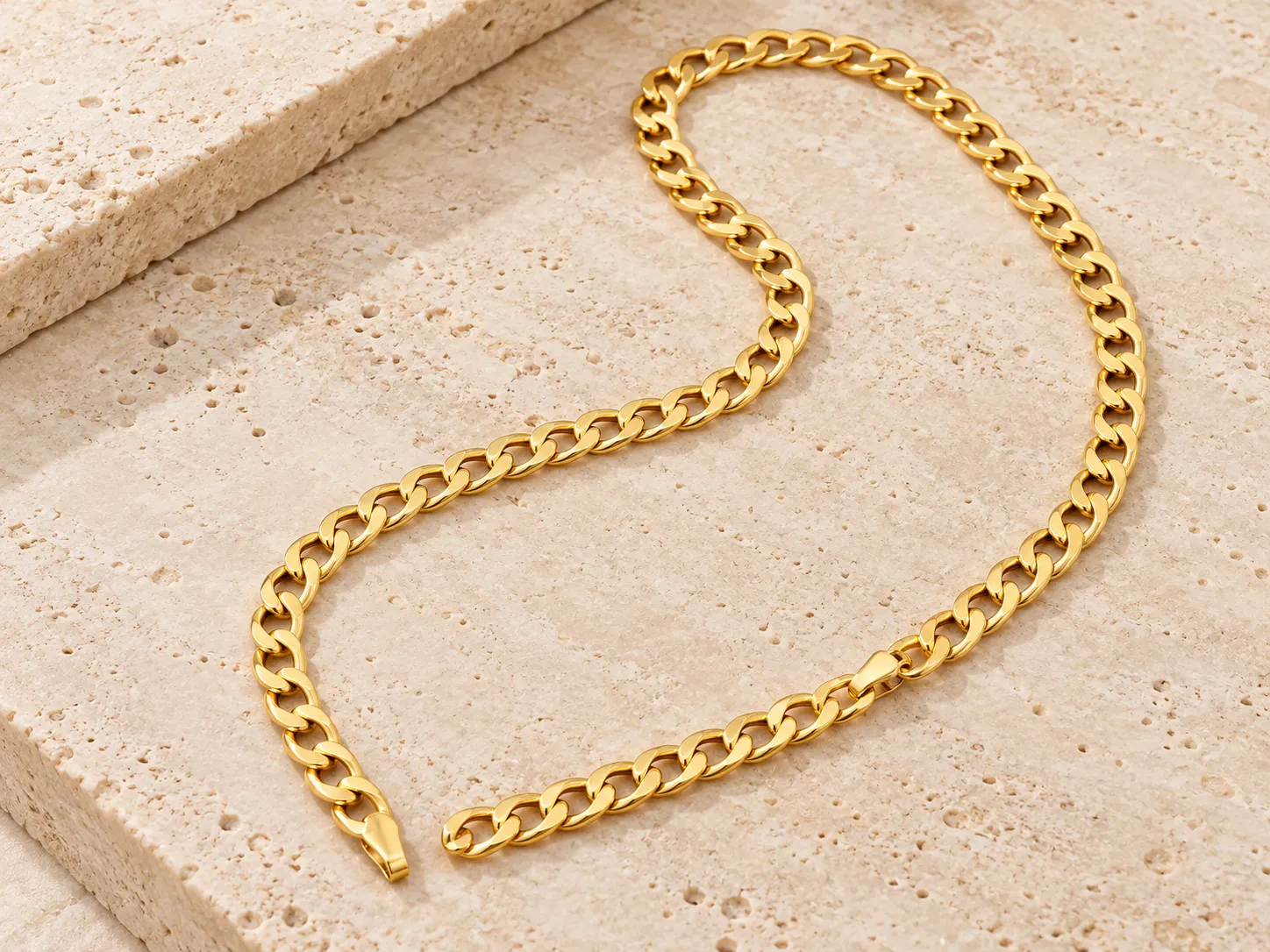 Broad gold curb chain laid in a curve on a stone ledge