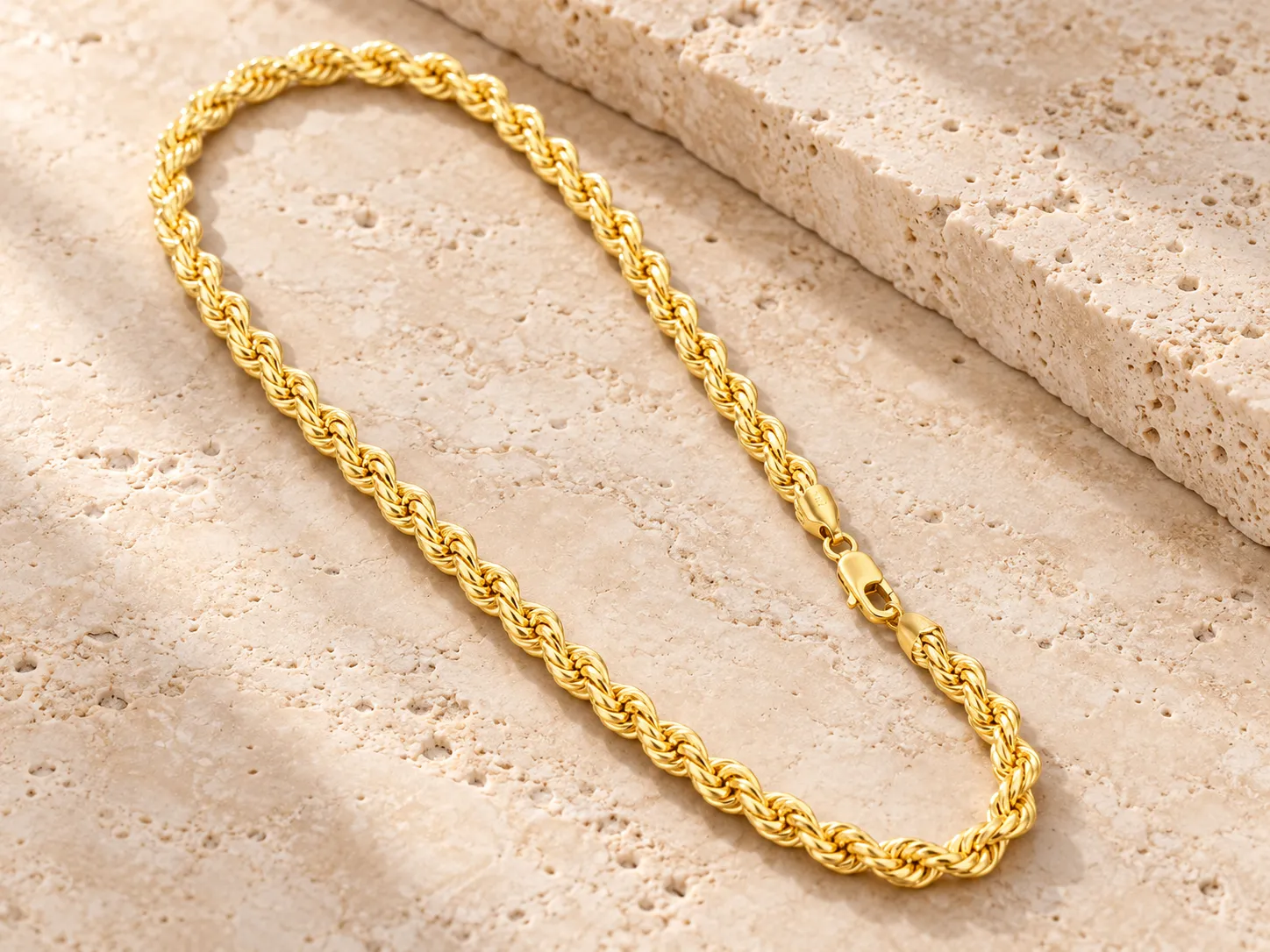 Thick gold twisted rope chain laid in a loop on a stone ledge