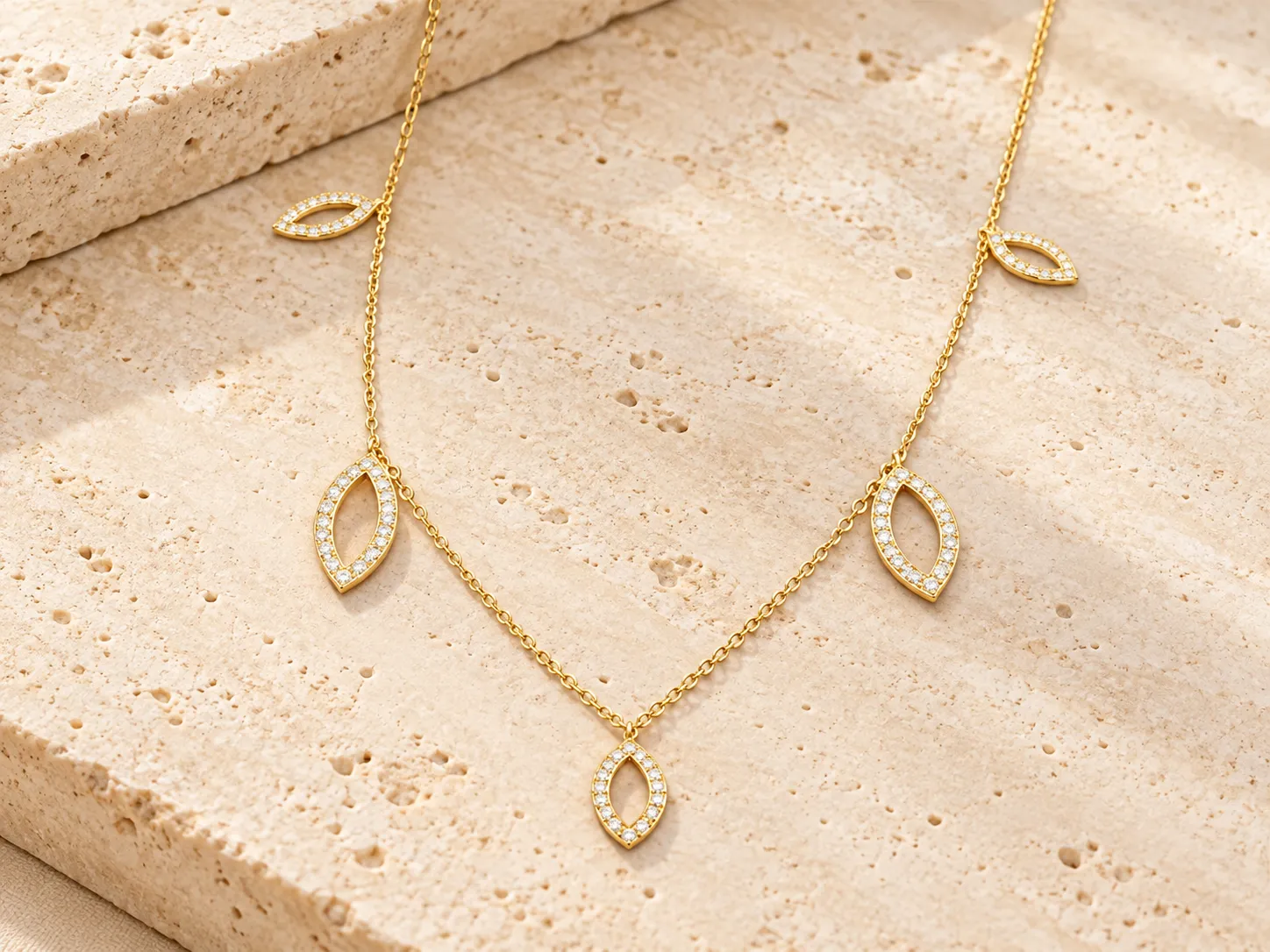 Fine gold chain with marquise-shaped charms outlined in small clear stones, resting on a stone ledge