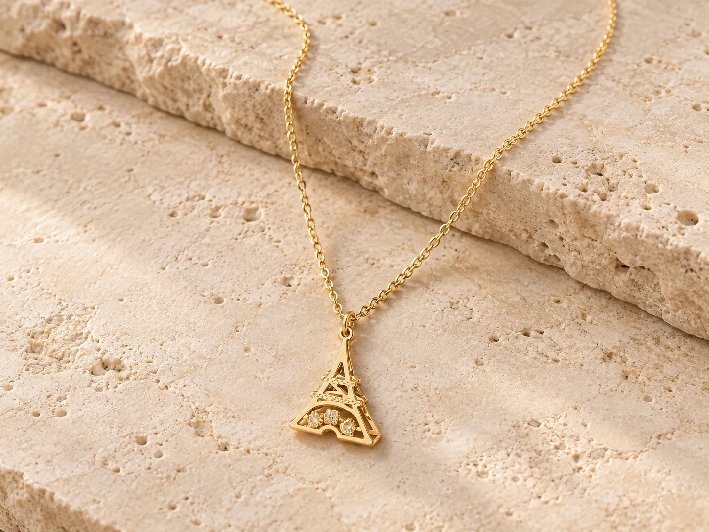 Gold necklace with an openwork Eiffel Tower pendant on a fine curb chain, resting on a stone ledge