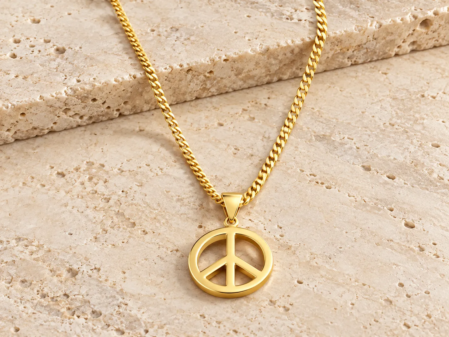 Gold necklace with a round peace-symbol pendant on a curb chain, resting on a stone ledge