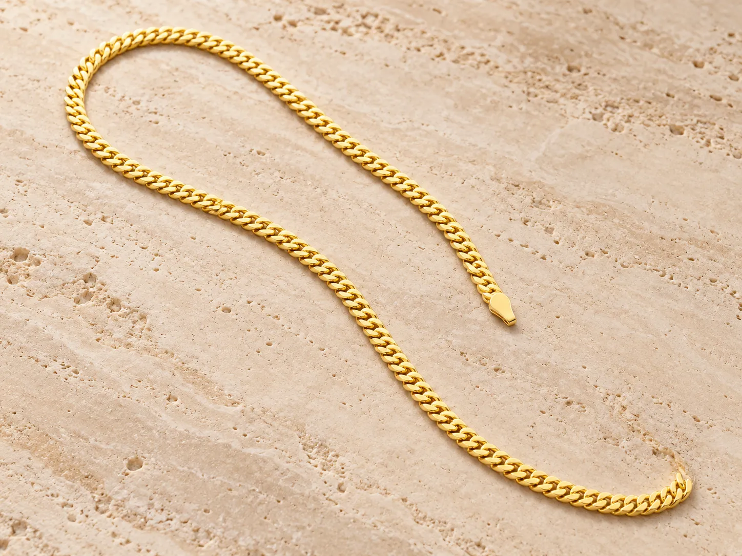 Flat gold curb chain laid in a long curve on a stone surface