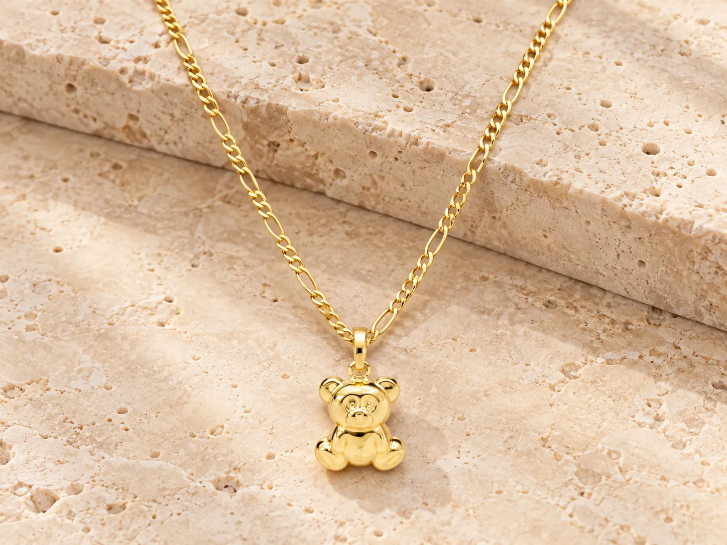 Gold necklace with a small teddy bear pendant on a fine chain, resting on a stone ledge