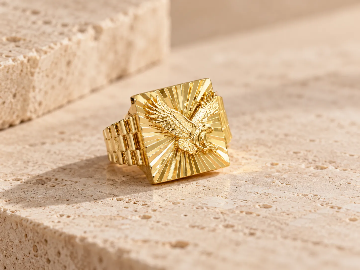 Gold signet ring with a raised eagle on a square face with radiating lines and a link-style band, on a stone ledge