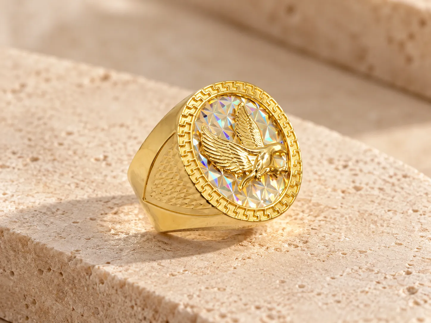 Gold signet ring with an eagle on a prismatic oval face with a decorative border and textured shoulders, on a stone ledge