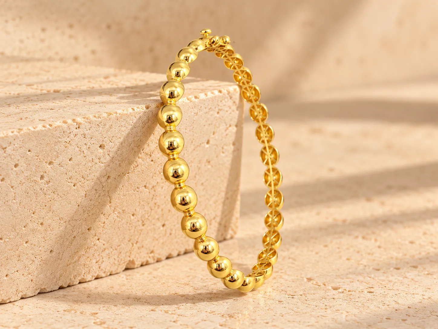 Gold bangle of polished round beads with a clasp, leaning on a stone block