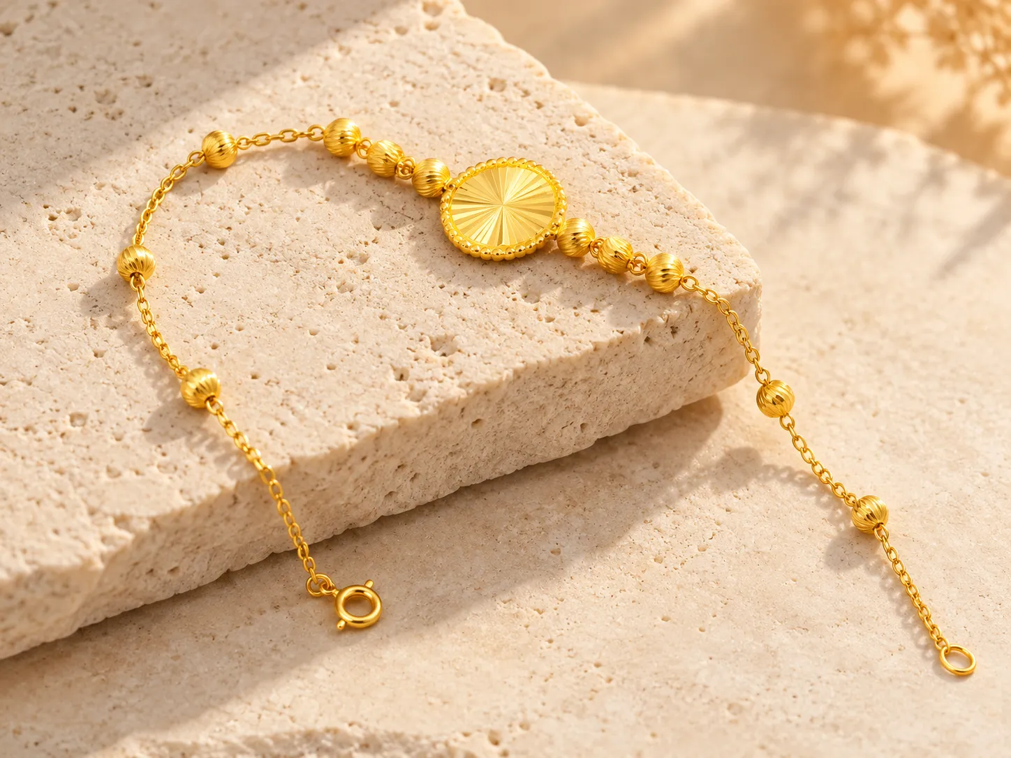 Gold bracelet with an oval motif and small round beads on a fine chain, on a stone slab