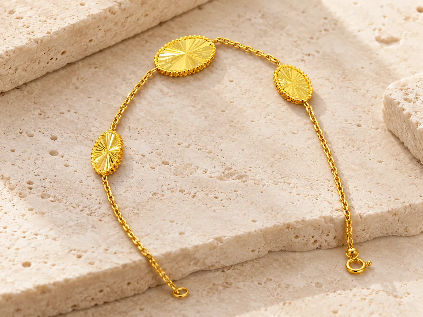 Gold bracelet with three oval motifs on a fine chain, on a stone surface