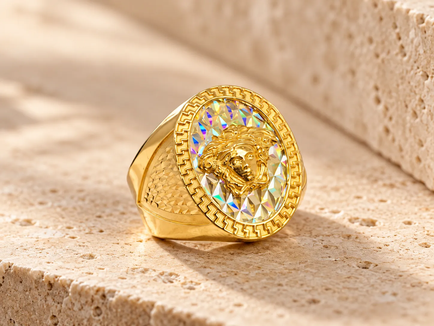 Gold signet ring with a sculpted head on a prismatic oval face with a Greek-key border and textured shoulders, on a stone ledge