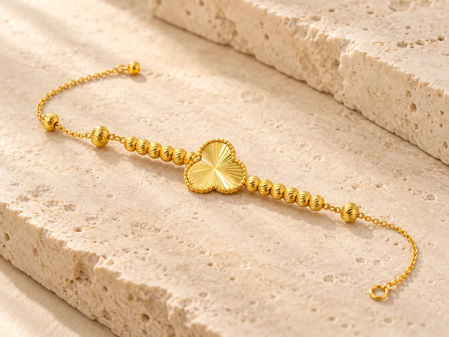 Gold bracelet with a clover-shaped motif and a row of small round beads on a fine chain, on a stone slab