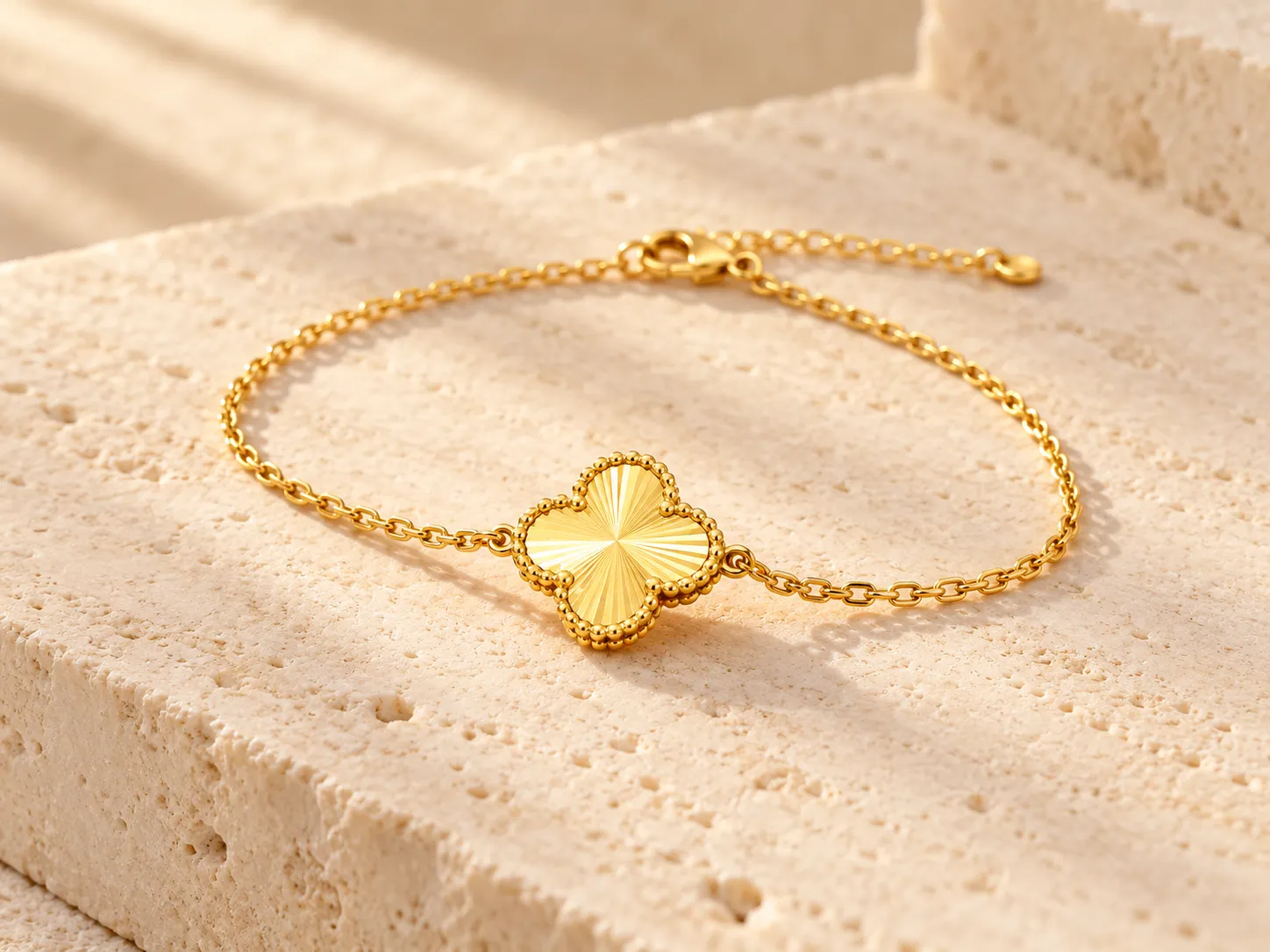 Gold bracelet with a single four-leaf clover motif on a fine chain, on a stone surface