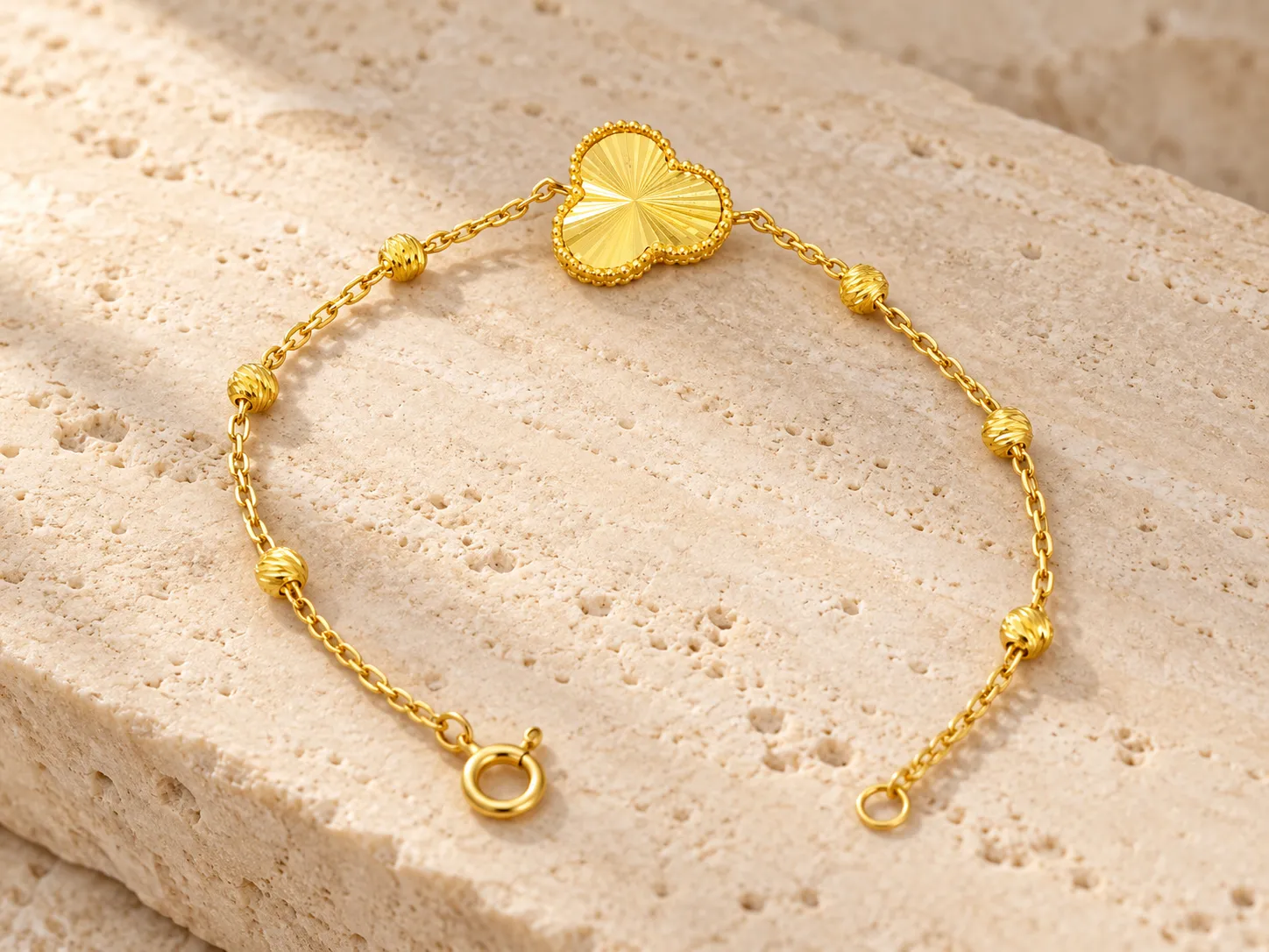 Gold bracelet with a clover-shaped motif and small round beads on a fine chain, on a stone surface