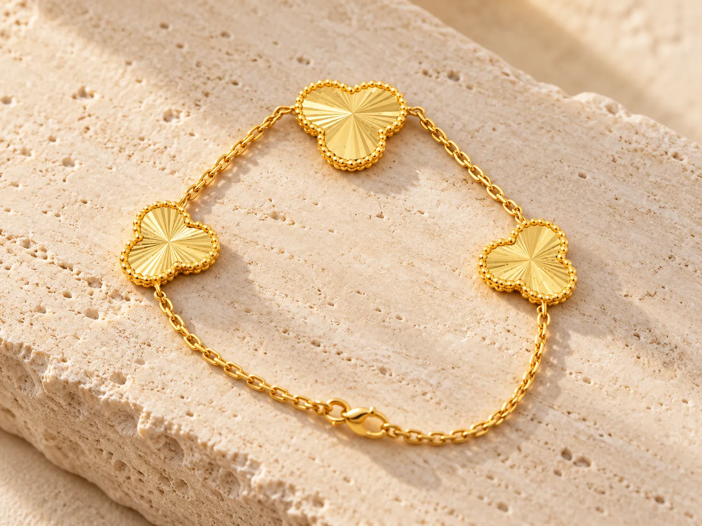 Gold bracelet with three clover-shaped motifs on a fine chain, on a stone surface
