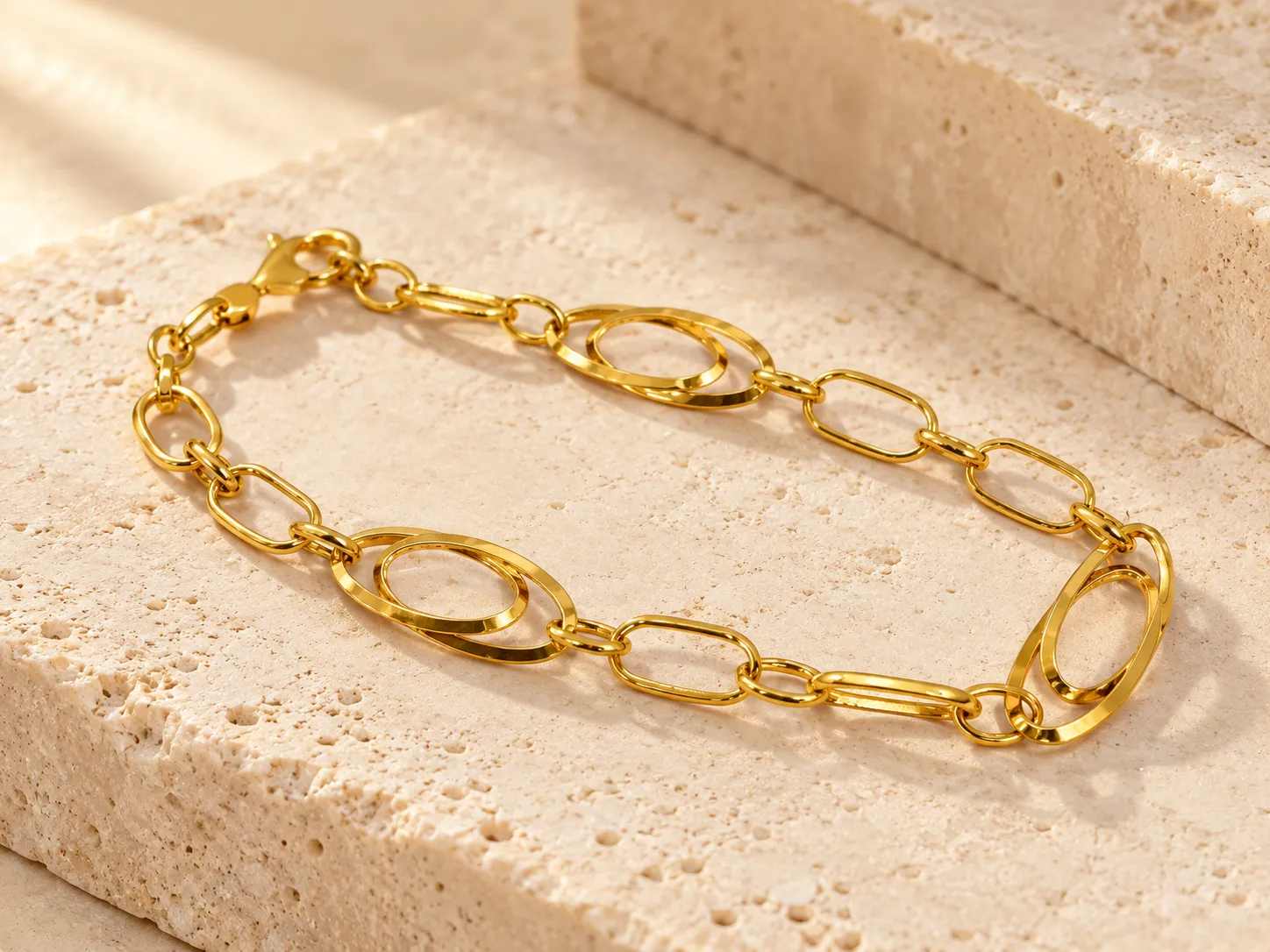 Gold bracelet with large oval links and slim rectangular links, on a stone slab