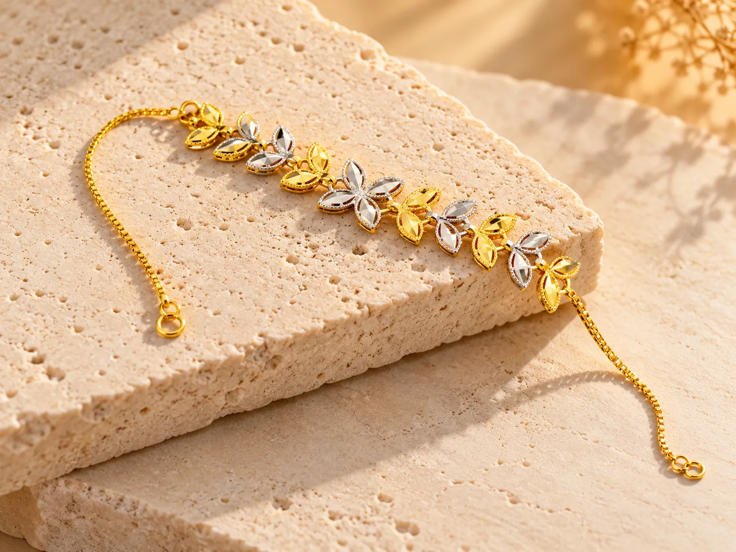 Gold bracelet with leaf and flower motifs, some silver-toned, on a fine chain, on a stone slab
