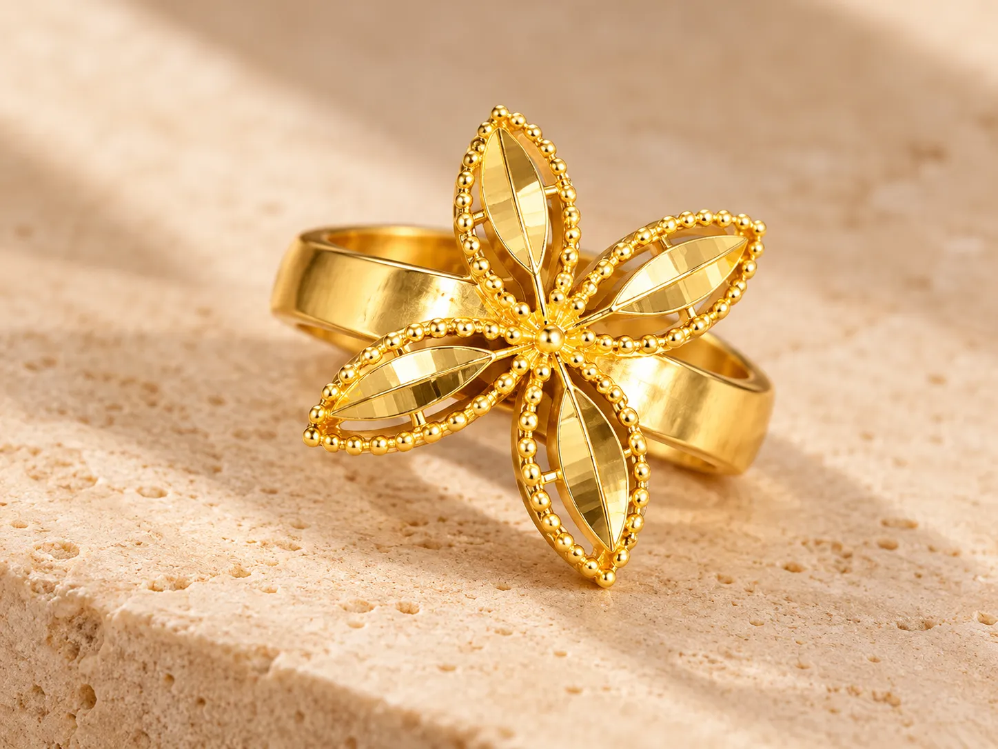Gold ring with a four-petal beaded openwork flower on a broad split band, on a stone ledge