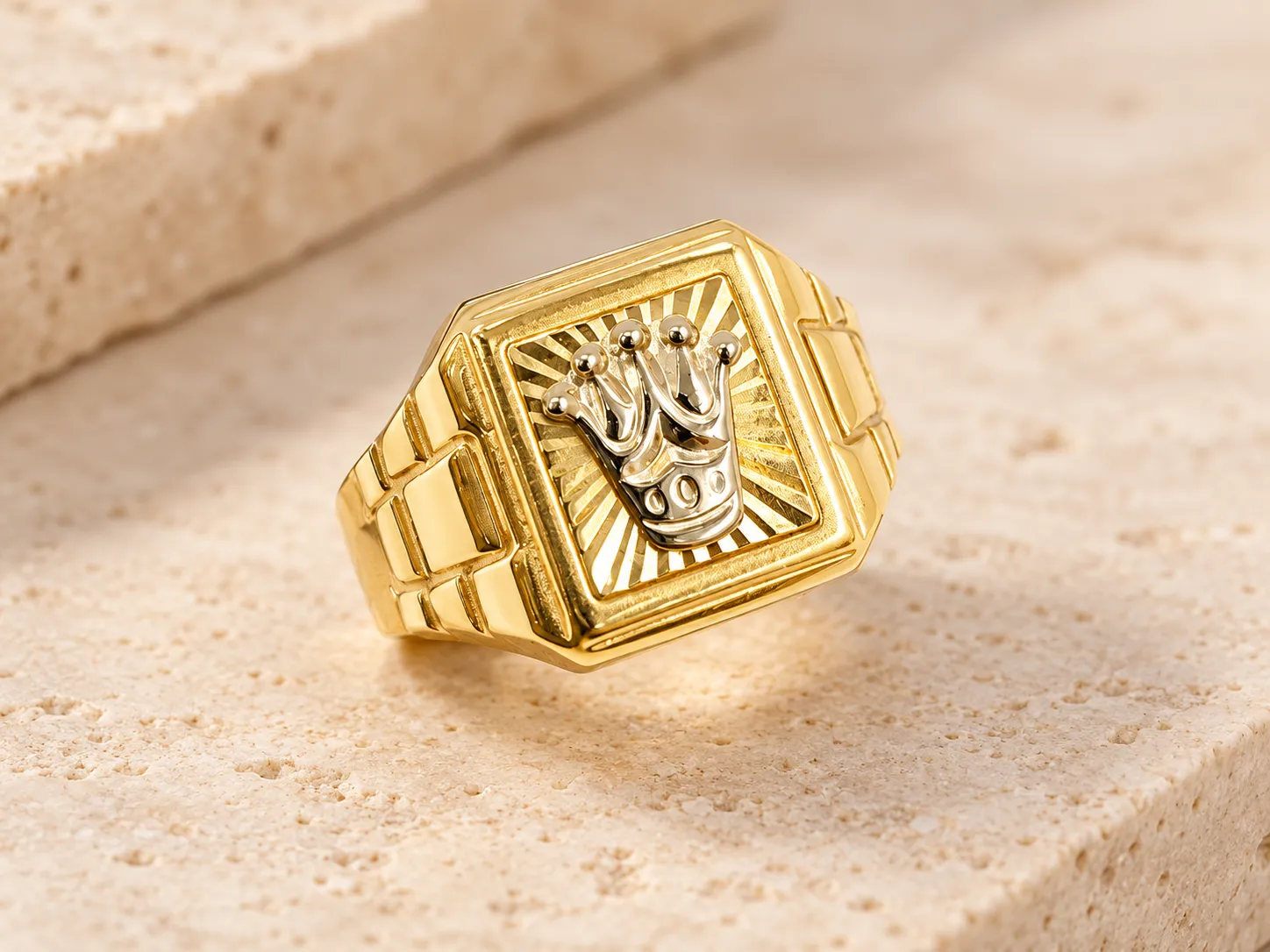 Gold signet ring with a silver-toned crown on a square face with radiating lines and link-style shoulders, on a stone ledge