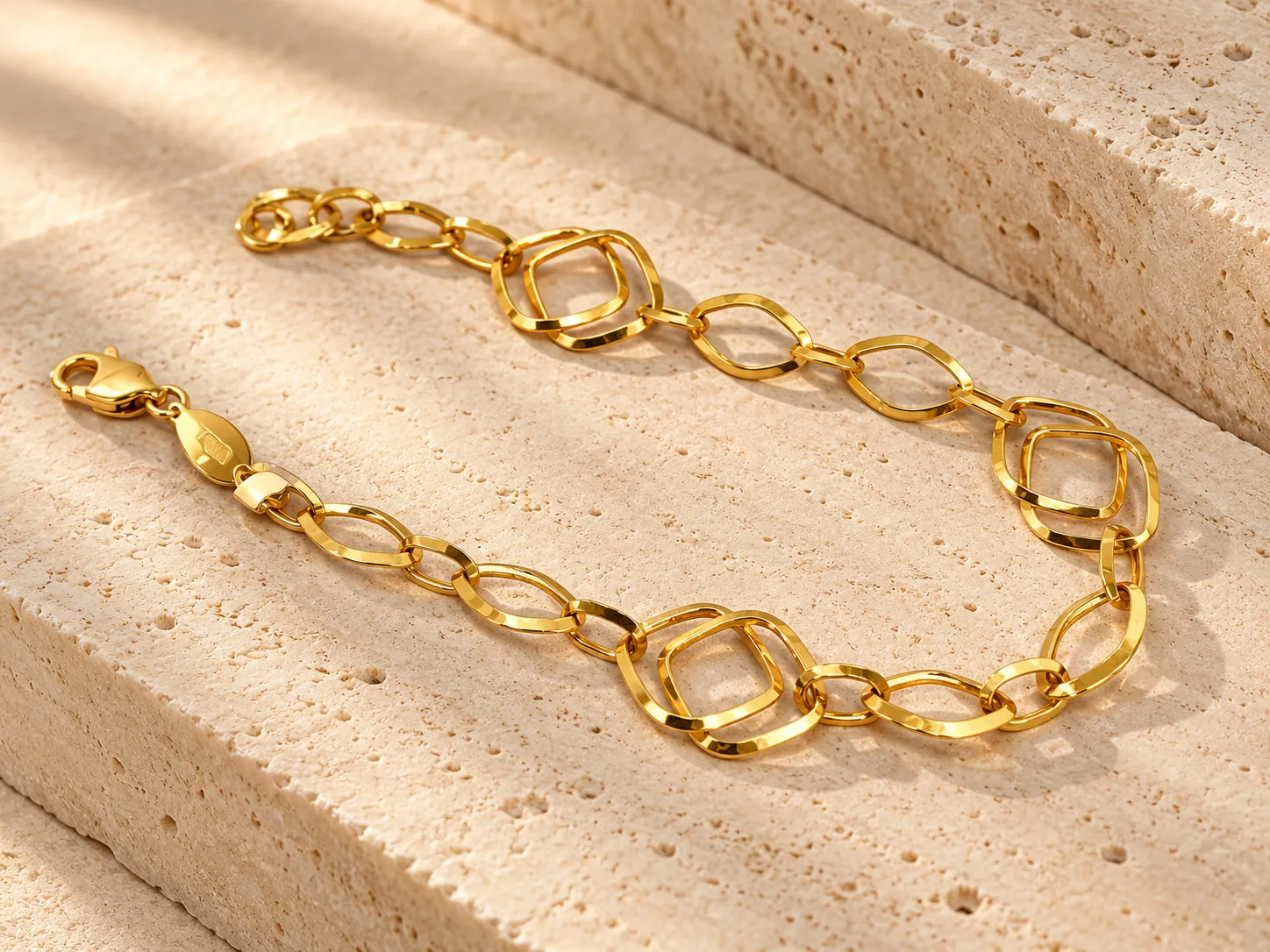 Gold bracelet of open square-shaped links with slim marquise shapes, on a stone slab