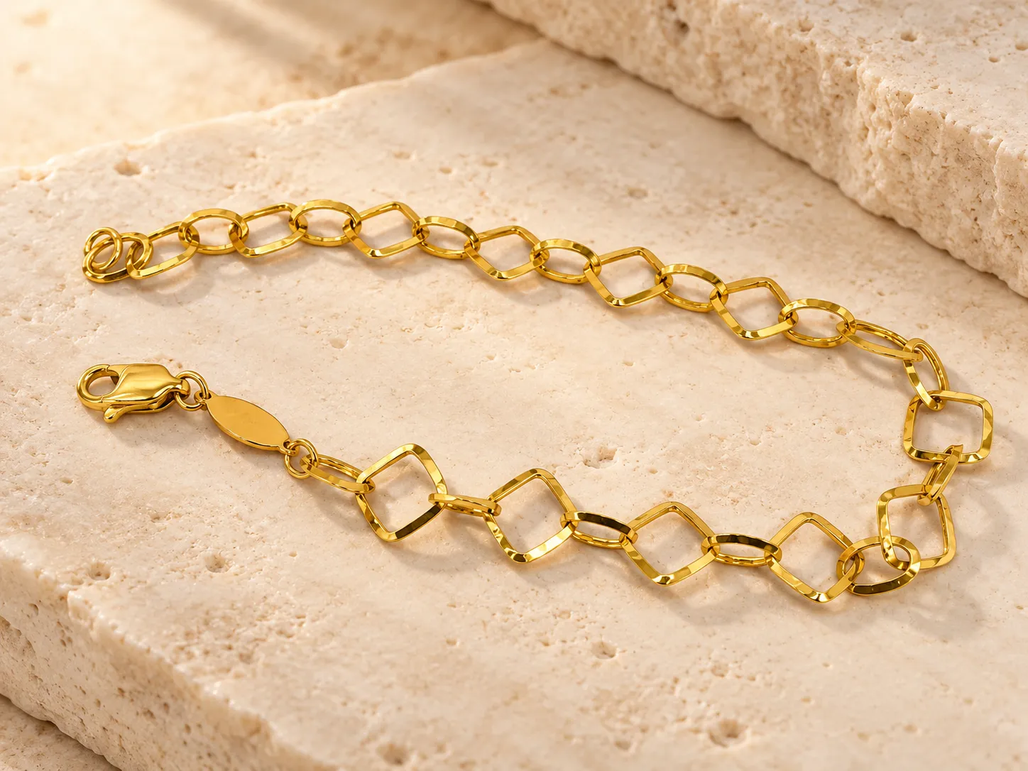 Gold bracelet of small open square-shaped links, on a stone slab