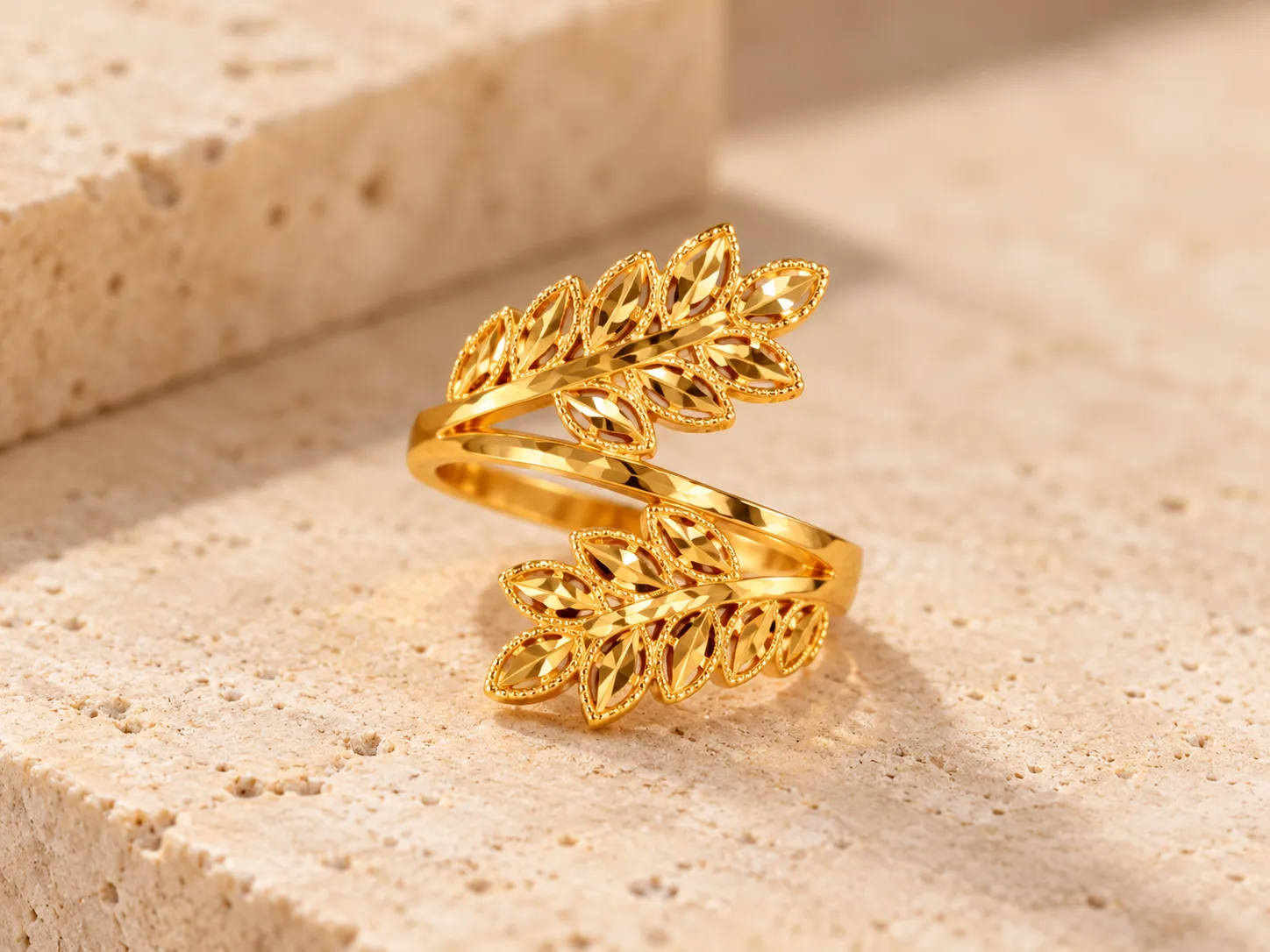 Open gold wrap ring with two textured laurel-style leaf branches, on a stone ledge