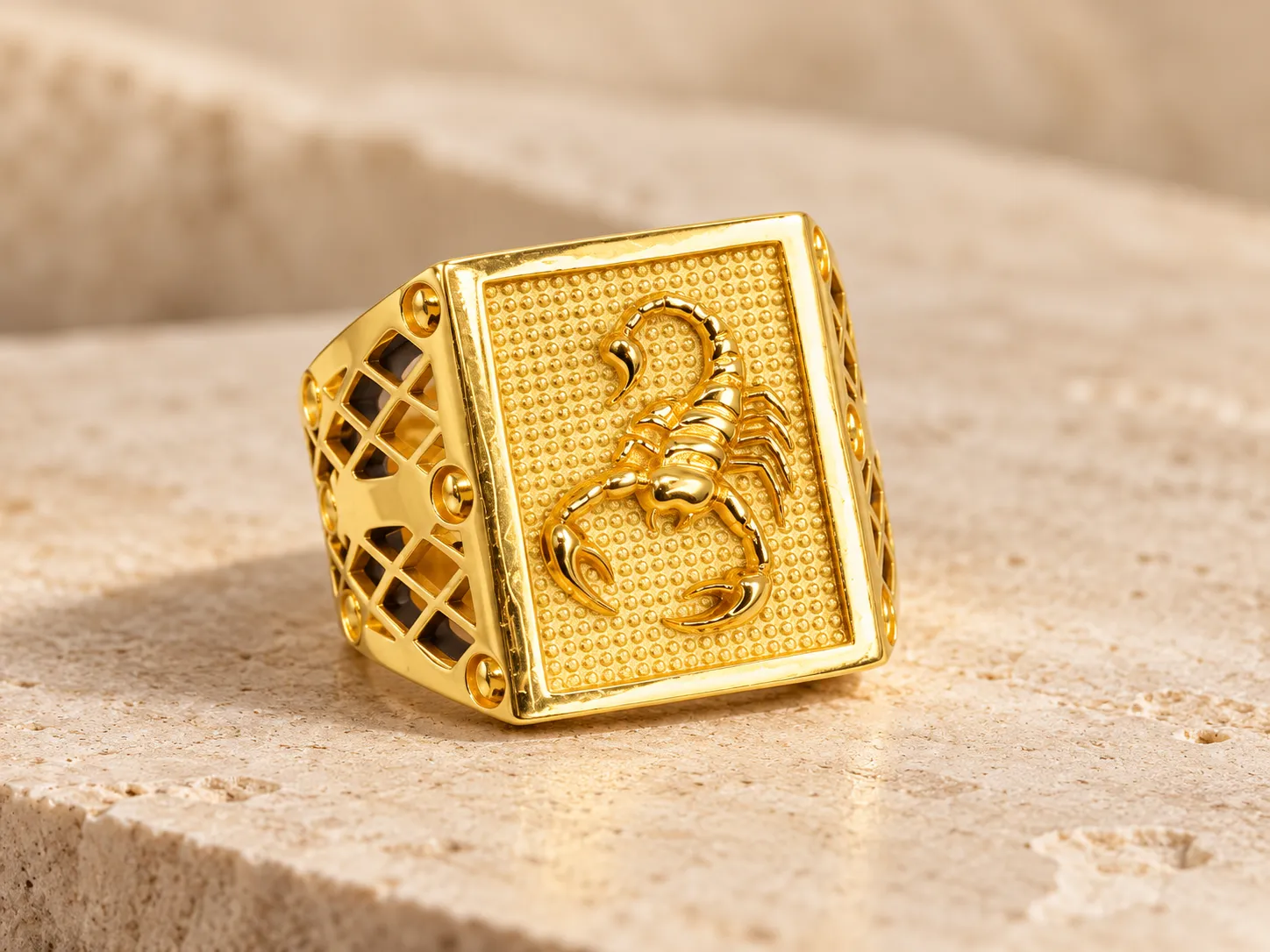 Gold signet ring with a raised scorpion on a dotted rectangular face and pierced lattice shoulders, on a stone ledge
