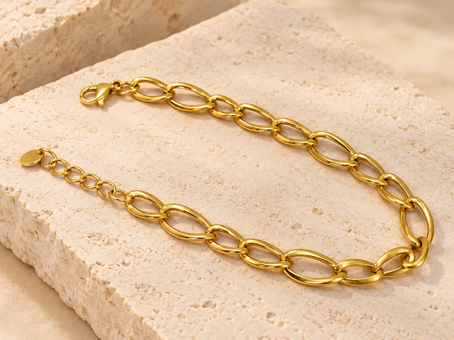 Gold bracelet of elongated polished oval links with a clasp and extension chain, on a stone slab