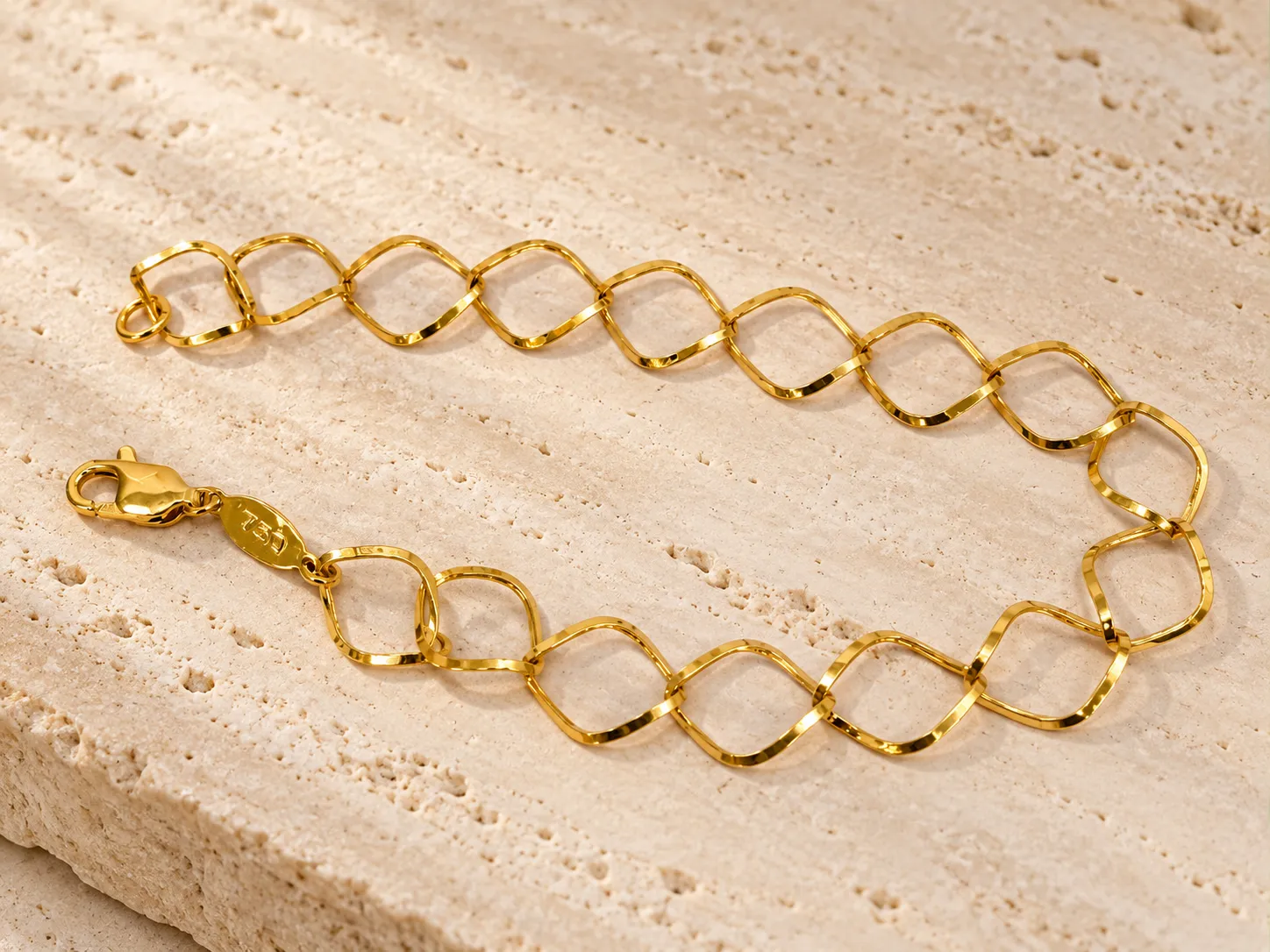 Gold bracelet of large open curved diamond-shaped links, on a stone slab