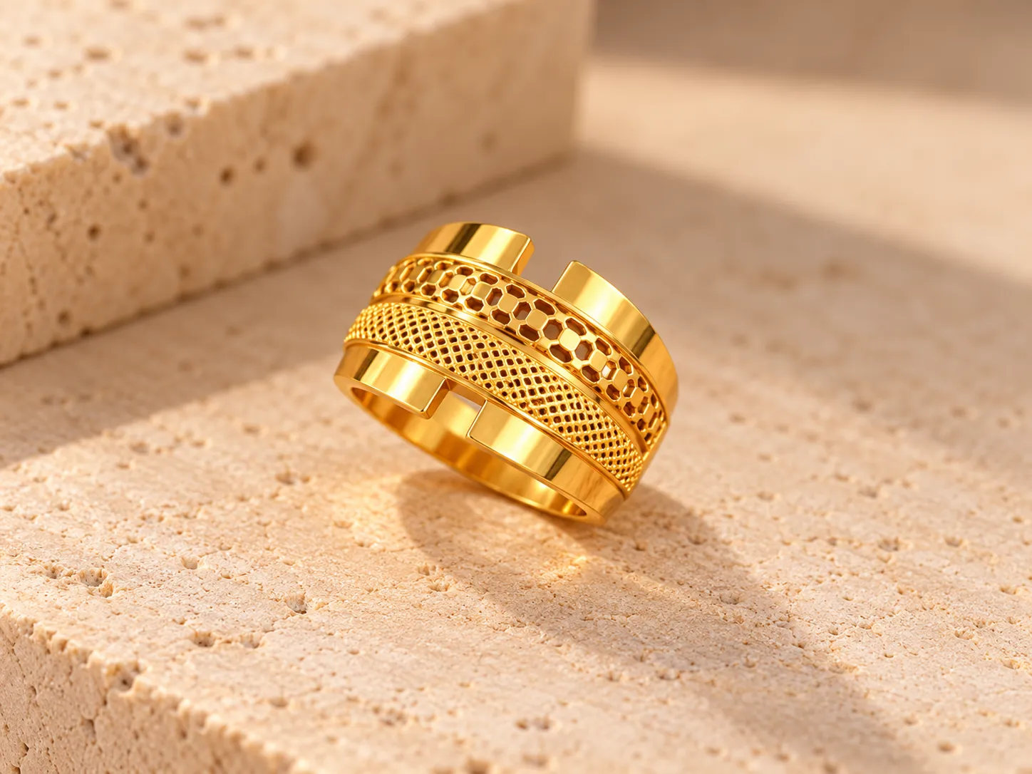 Broad gold ring with a honeycomb openwork panel and a fine mesh panel between polished gold plates, on a stone ledge