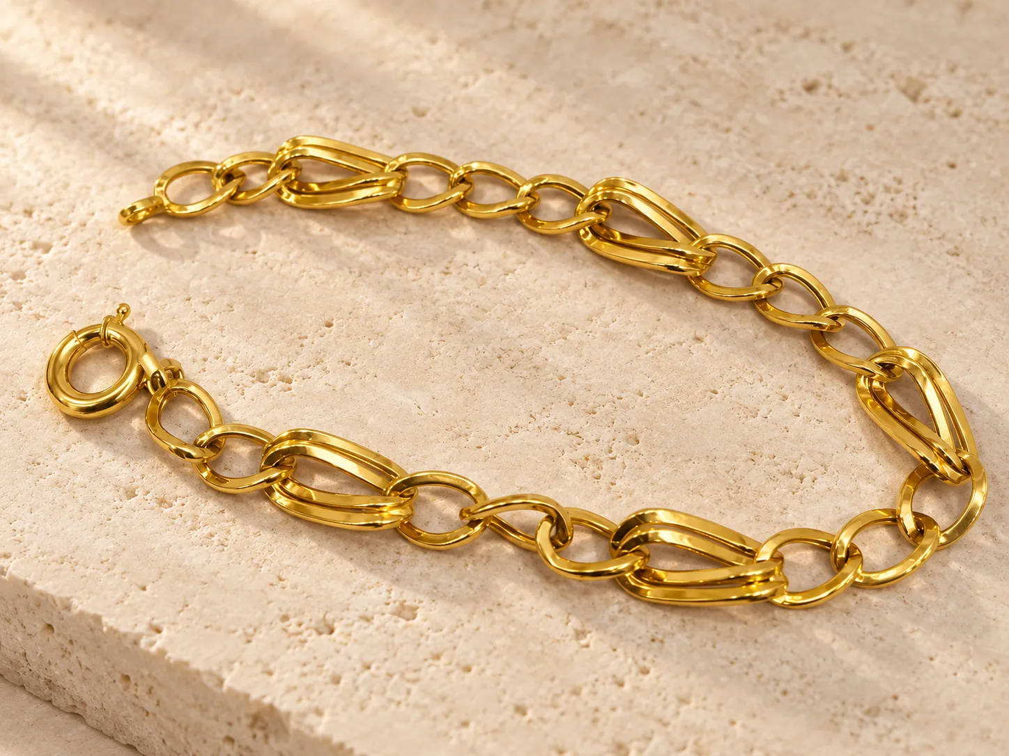Gold bracelet of heavy sculpted links with a ring clasp, on a stone slab