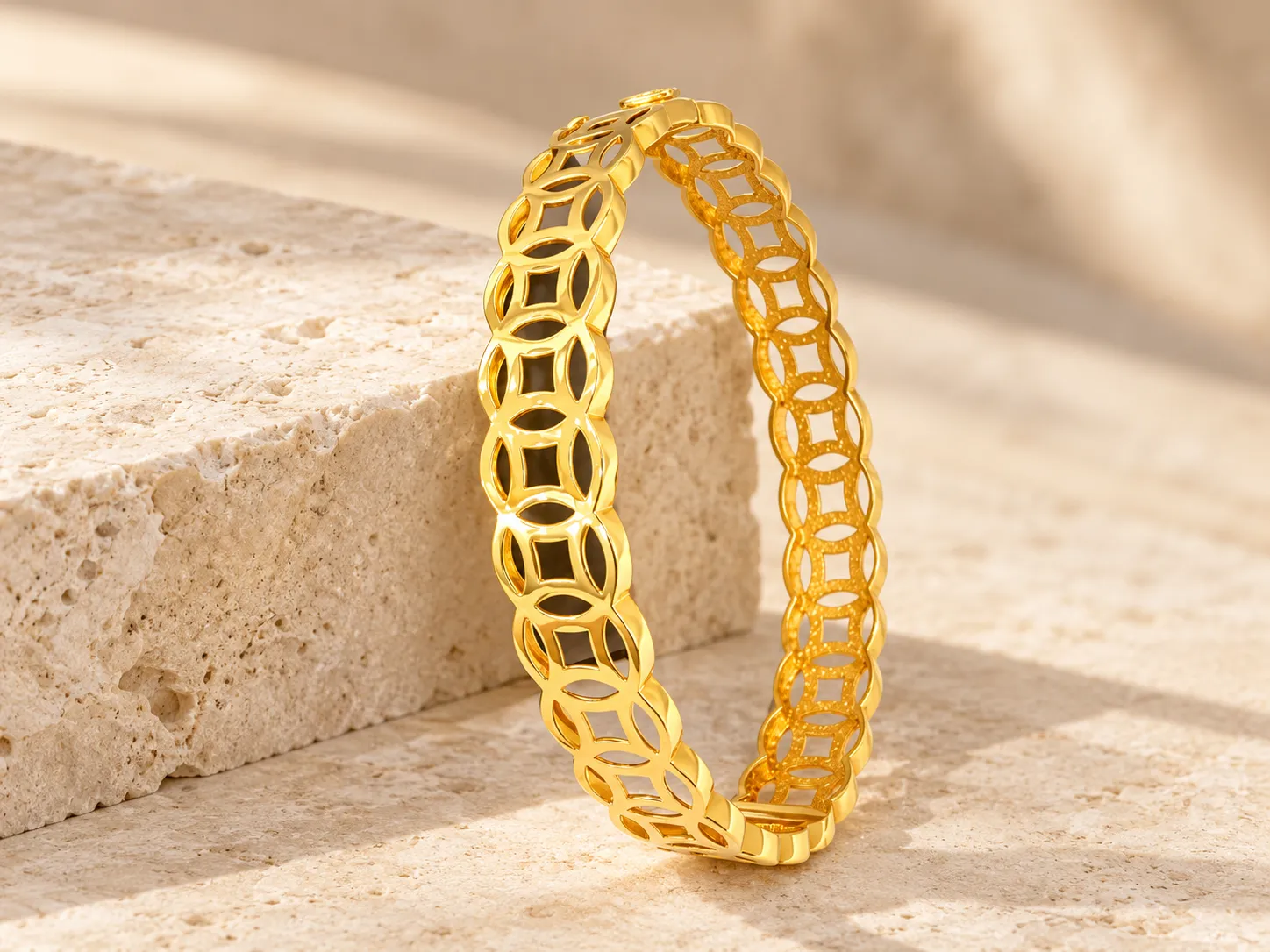 Broad gold bangle of interlocking circles with open square centres, standing on a stone ledge