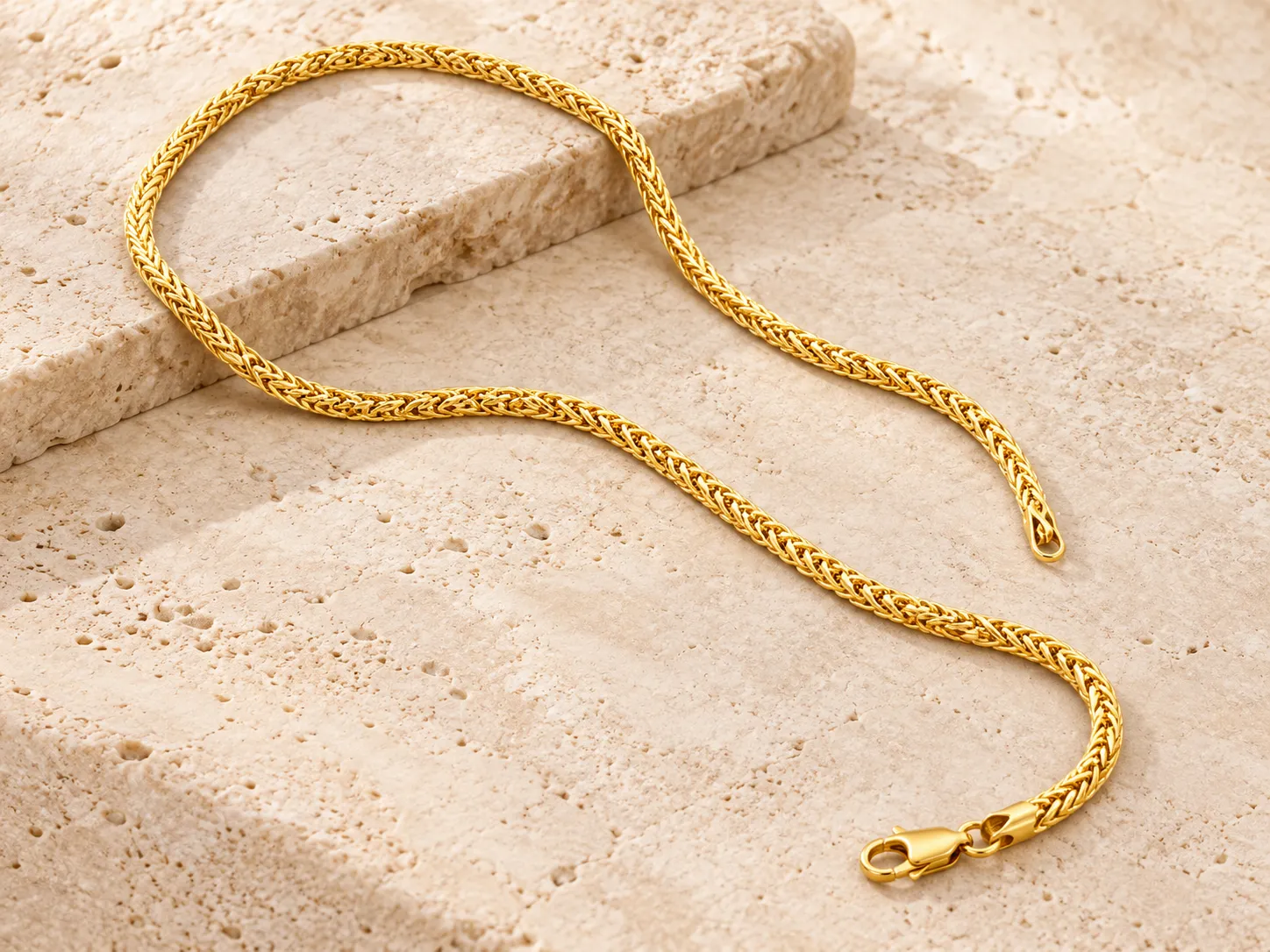 Gold woven-link chain with a clasp, laid in a curve on a stone ledge