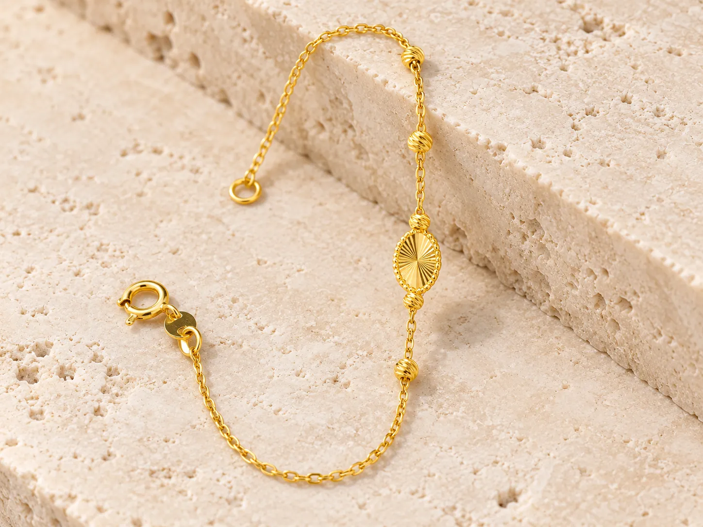 Gold bracelet with a fine chain, small beads and an oval centre piece on a warm stone surface
