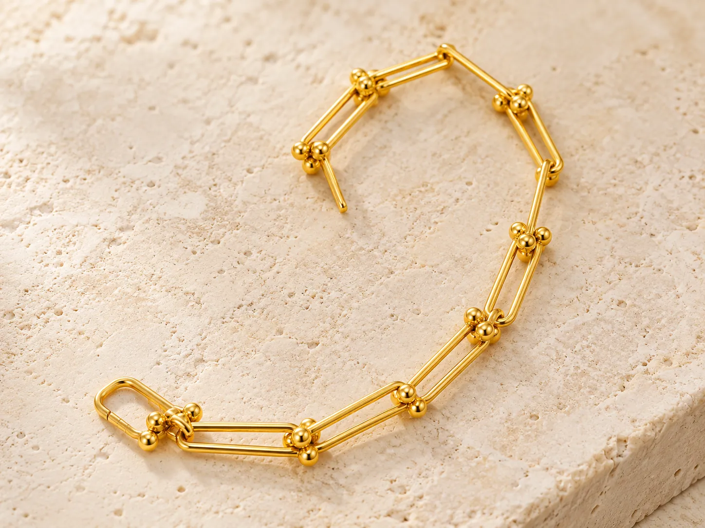 Gold link bracelet with beaded joints on a warm stone surface