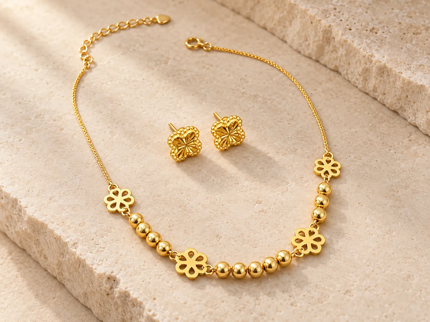 Gold chain bracelet with beads and flower motifs beside a pair of clover-shaped earrings