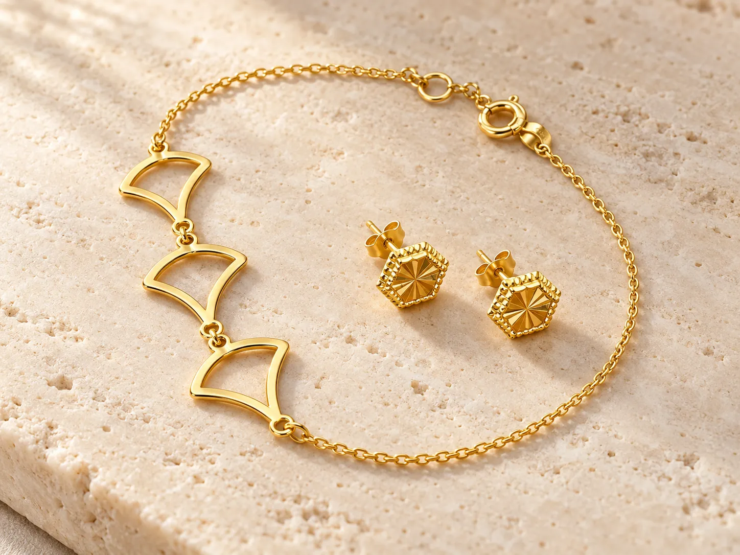 Gold bracelet with open fan-shaped links beside a pair of hexagonal earrings