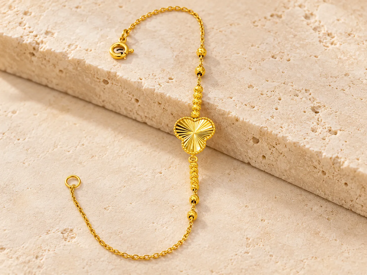 Gold bracelet with a round textured centre piece and beads, photographed on a warm stone step