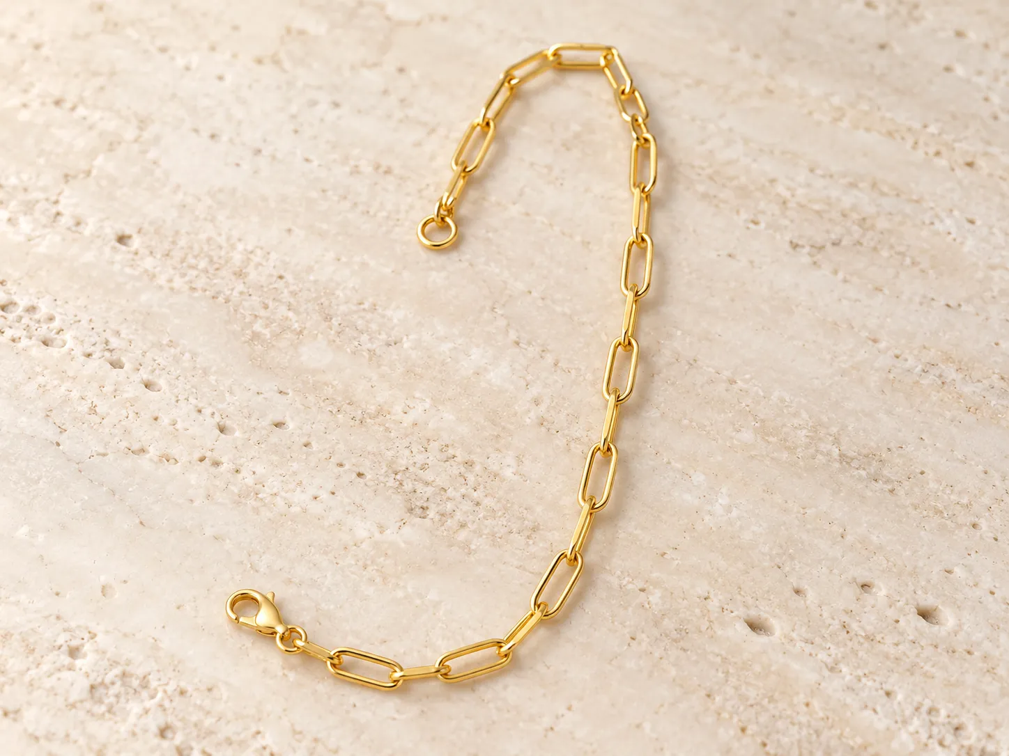 Gold paperclip-chain bracelet photographed on a warm stone surface