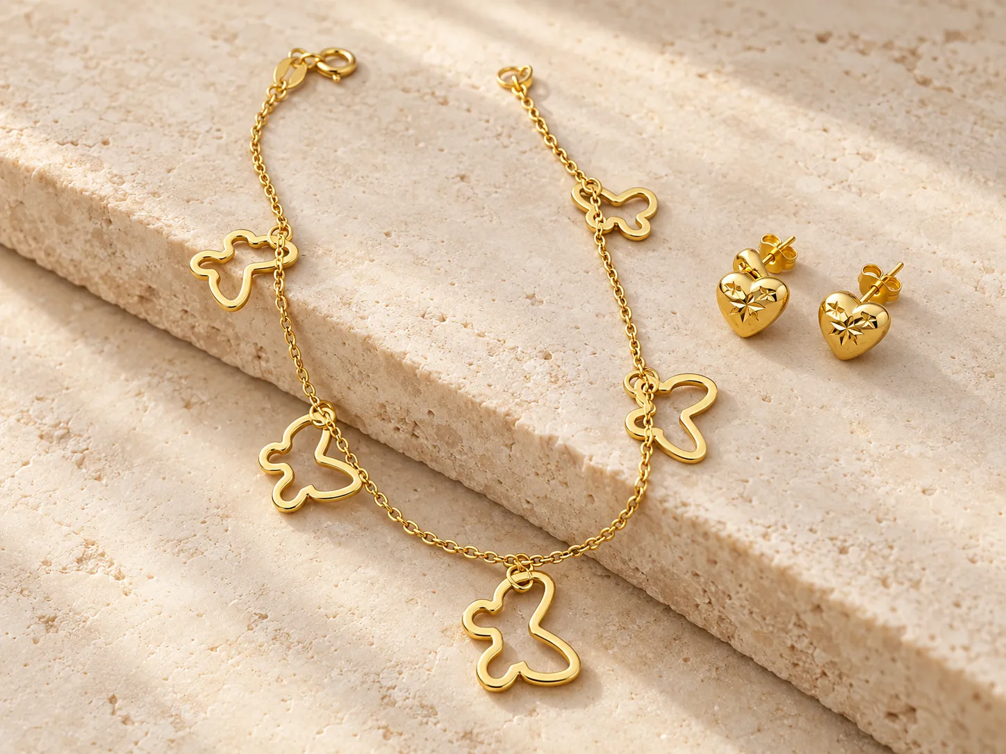 Gold charm bracelet with open butterfly charms beside a pair of heart-shaped earrings
