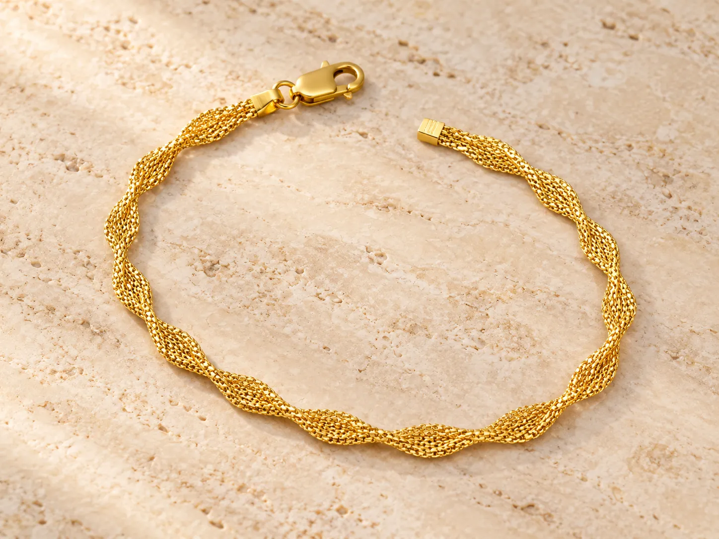 Gold twisted mesh bracelet with a clasp, photographed on a warm stone surface