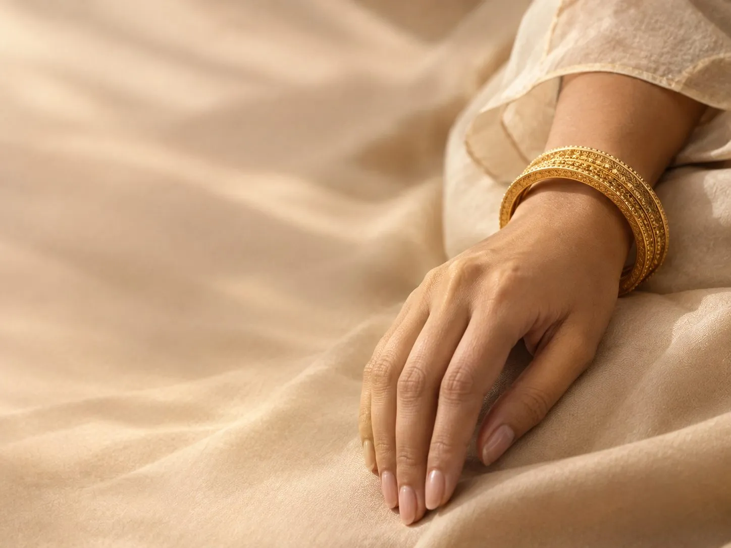 A hand wearing stacked engraved gold bangles, resting on ivory fabric