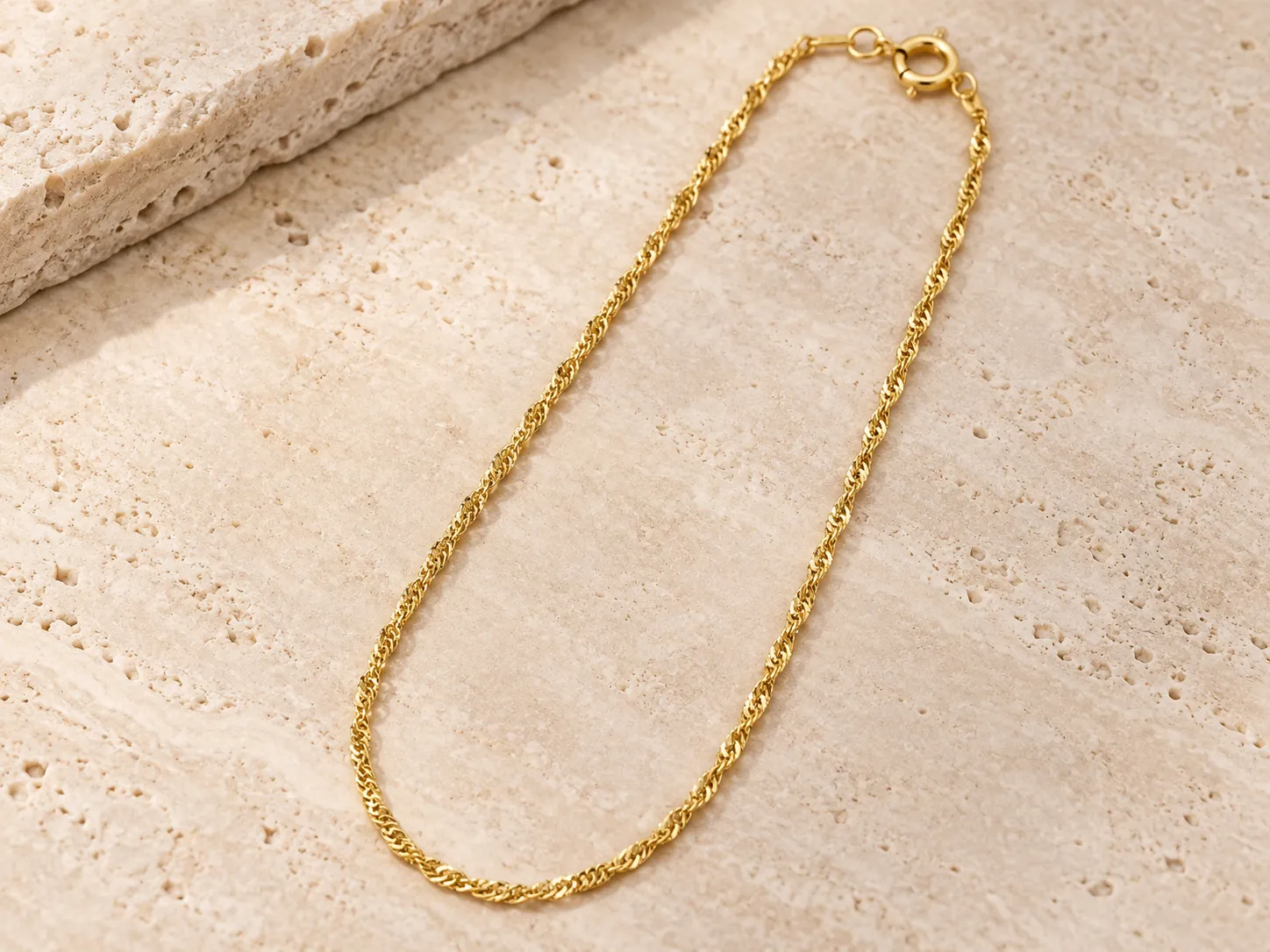 Gold twisted-link chain necklace laid on a warm stone surface