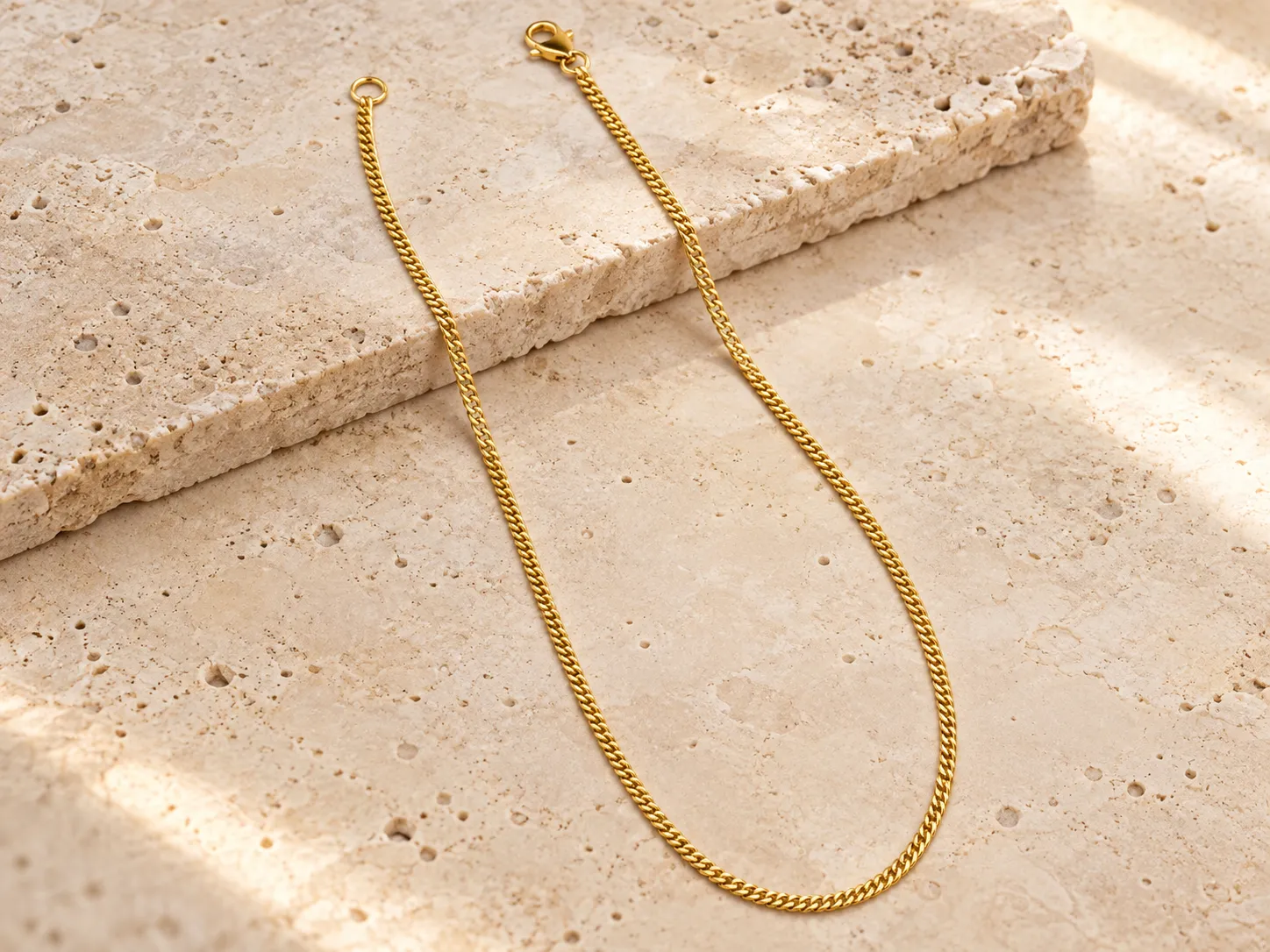 Fine gold curb-chain necklace draped over a stone ledge