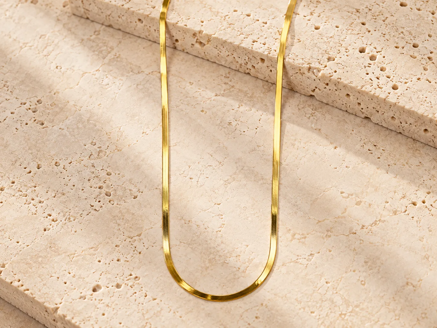 Flat gold chain necklace hanging over a stone ledge