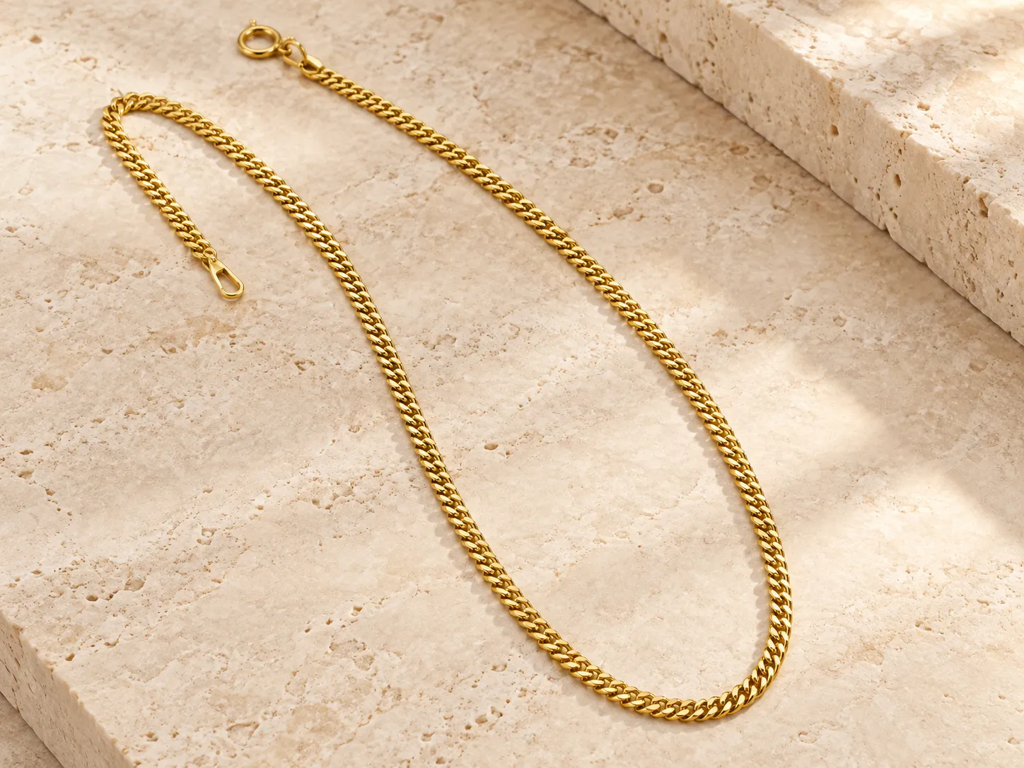 Gold curb-chain necklace with a clasp on a warm stone surface