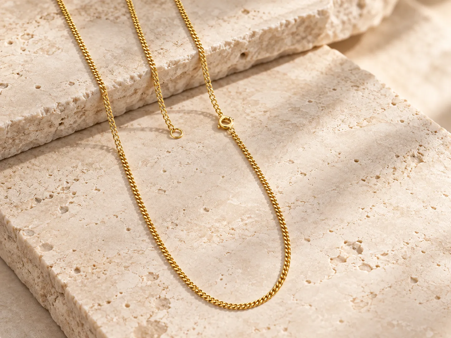 Fine gold curb-chain necklace draped over a stone ledge